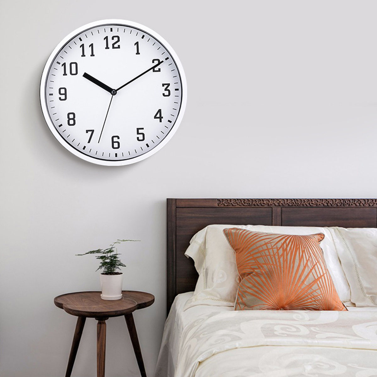 Eine weiße Wanduhr hängt über einem Holzbett mit einem orange gemusterten Kissen.
