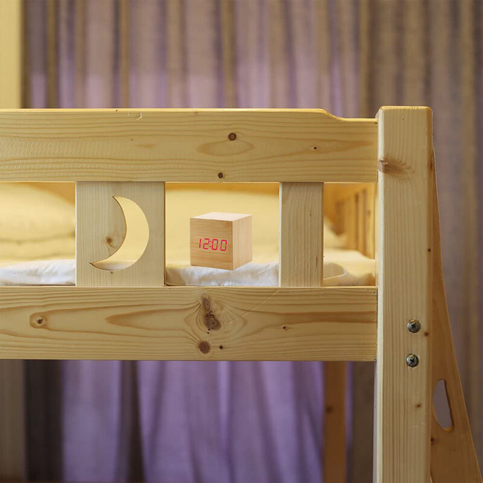 Ein Holzwecker mit roter Digitalanzeige (12:00) auf einem Bett.