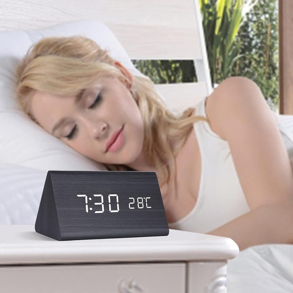 Eine Frau schläft, während eine Digitaluhr 7:30 und 28C anzeigt.