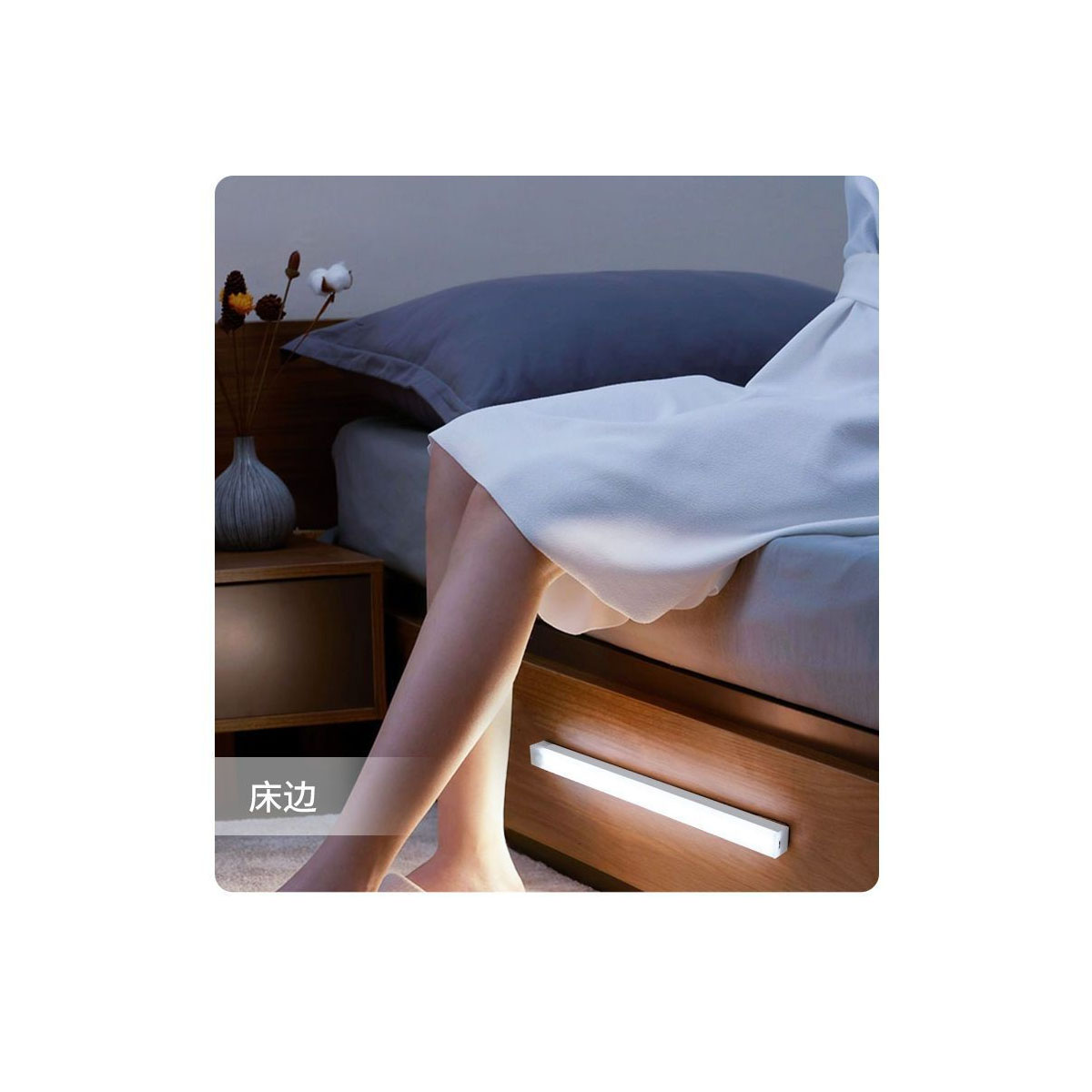 Person sitzt auf Bett mit weißem Rock, Nachttischlampe an, Vase mit Blumen.