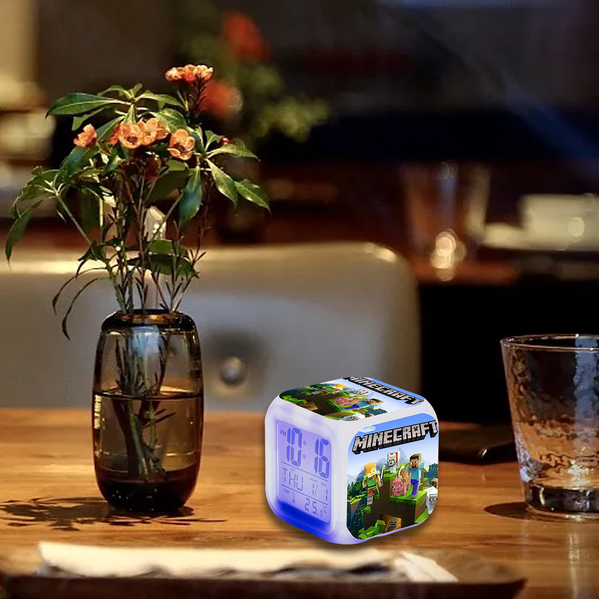 Minecraft-Würfeluhr auf einem Holztisch neben einer Vase mit Blumen.
