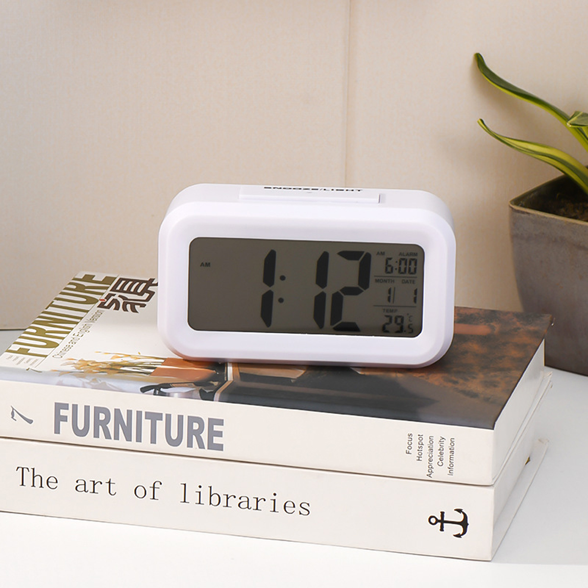 Ein weißer Digitalwecker zeigt 1:12 Uhr, 6:00 Uhr Alarm und 29,8°C an.