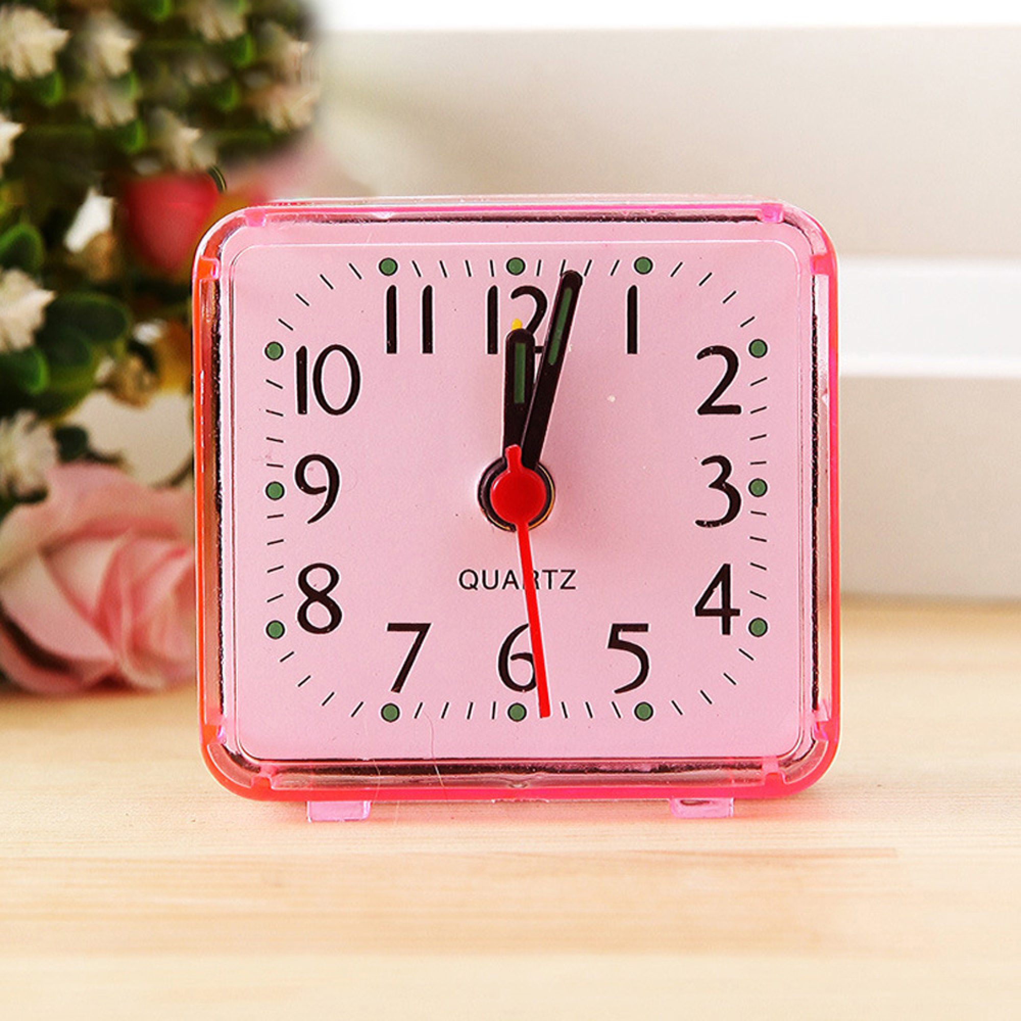 Ein kleiner pinker Wecker mit roten und schwarzen Zeigern steht auf einem Holztisch.