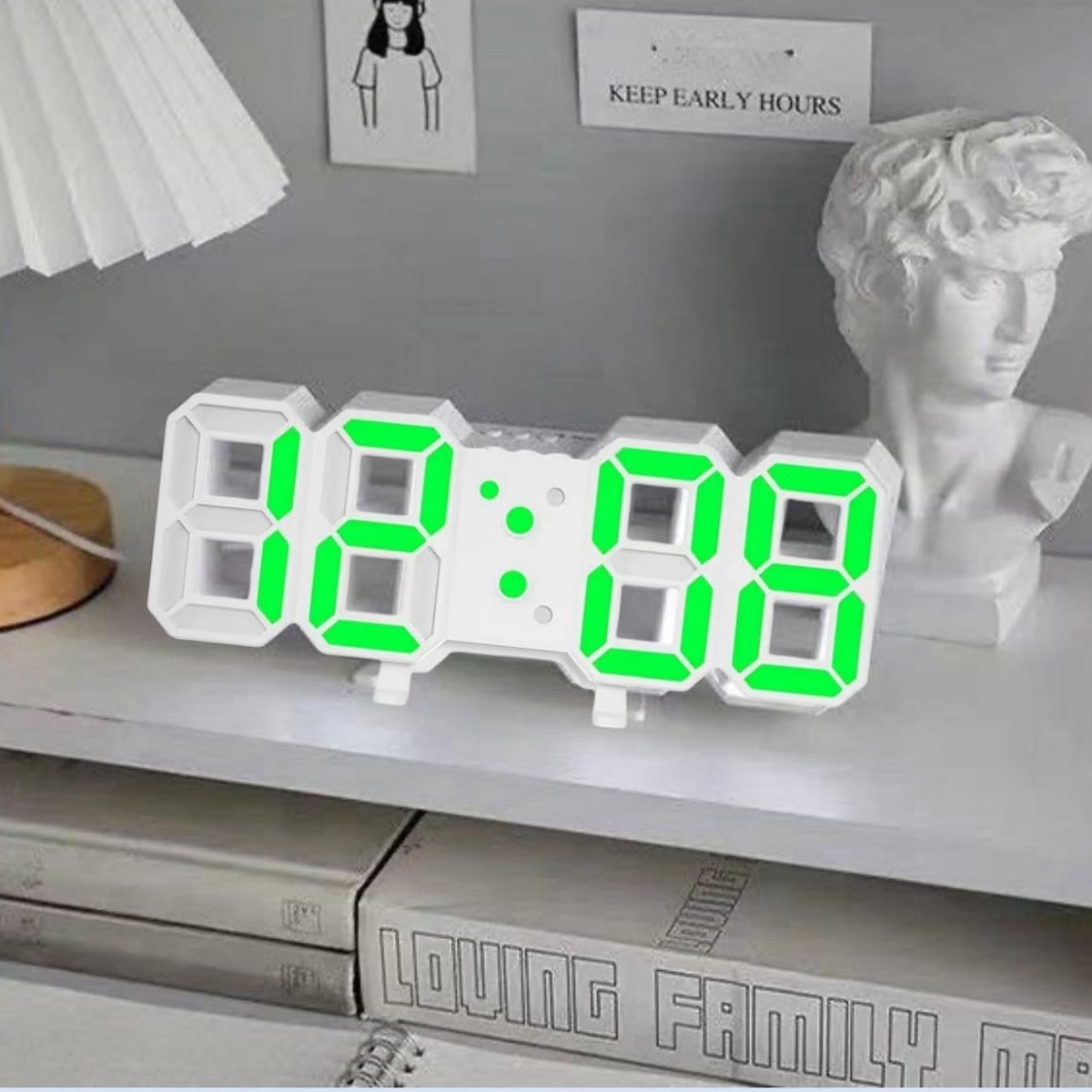 Eine weiße Digitaluhr mit grünen Zahlen zeigt 12:08 Uhr. Eine Büste ist rechts.