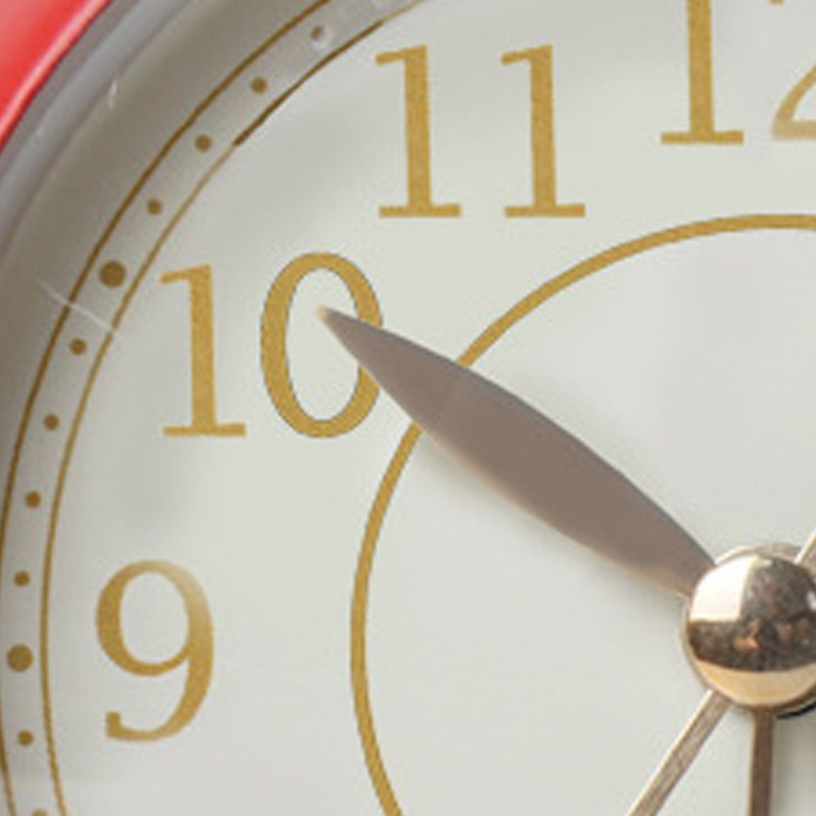 Nahaufnahme eines roten Weckers mit goldenen Ziffern und Zeigern, die auf fast 10 Uhr zeigen.