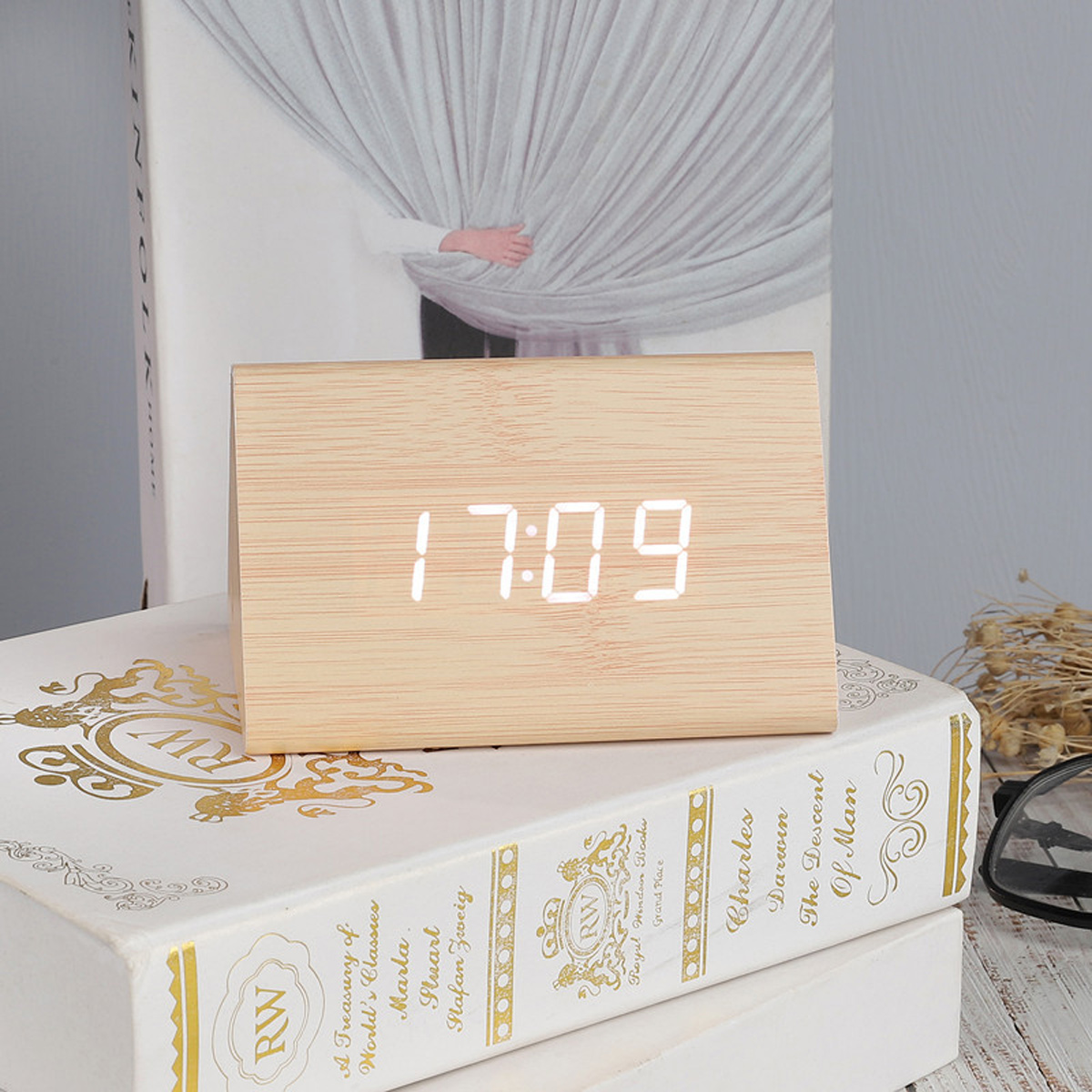 Eine hölzerne Digitaluhr mit der Anzeige 17:09 steht auf gestapelten Büchern.