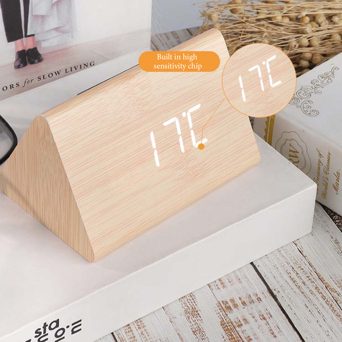 Ein hölzerner Digitalwecker zeigt 17°C an, daneben ein Buch und trockene Pflanzen.