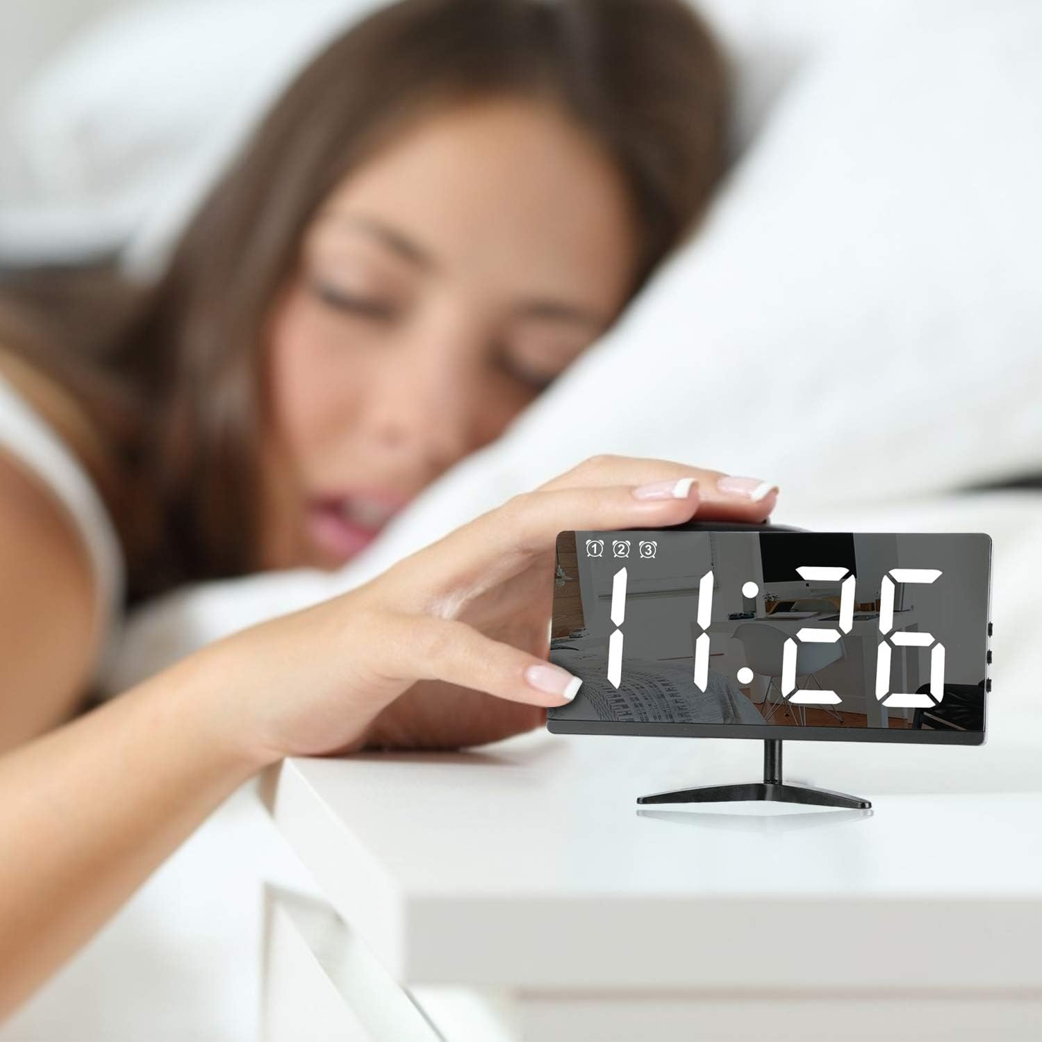 Frau schläft neben einem digitalen Wecker auf einem Nachttisch.