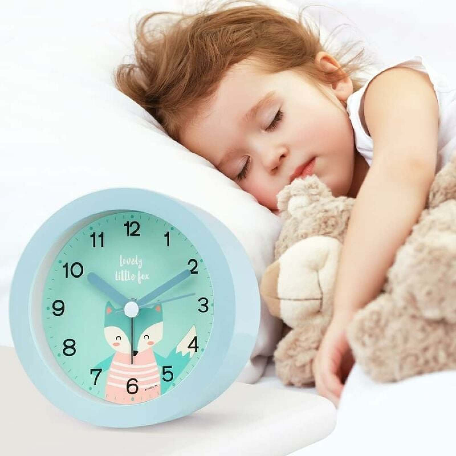 Ein kleines Kind schläft friedlich mit einem Teddybär, ein Nachttischwecker steht daneben.