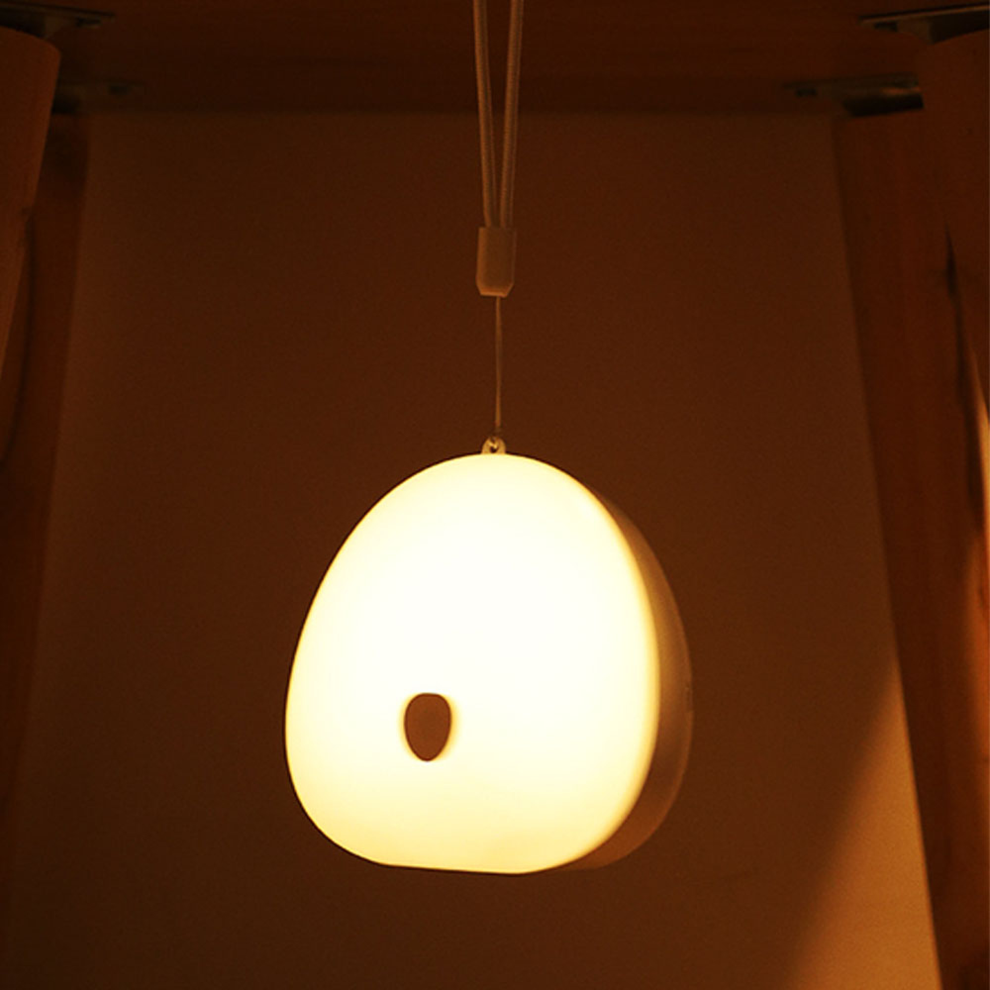 Eine runde, weiße Lampe mit einem dunklen Fleck hängt an einem Band.