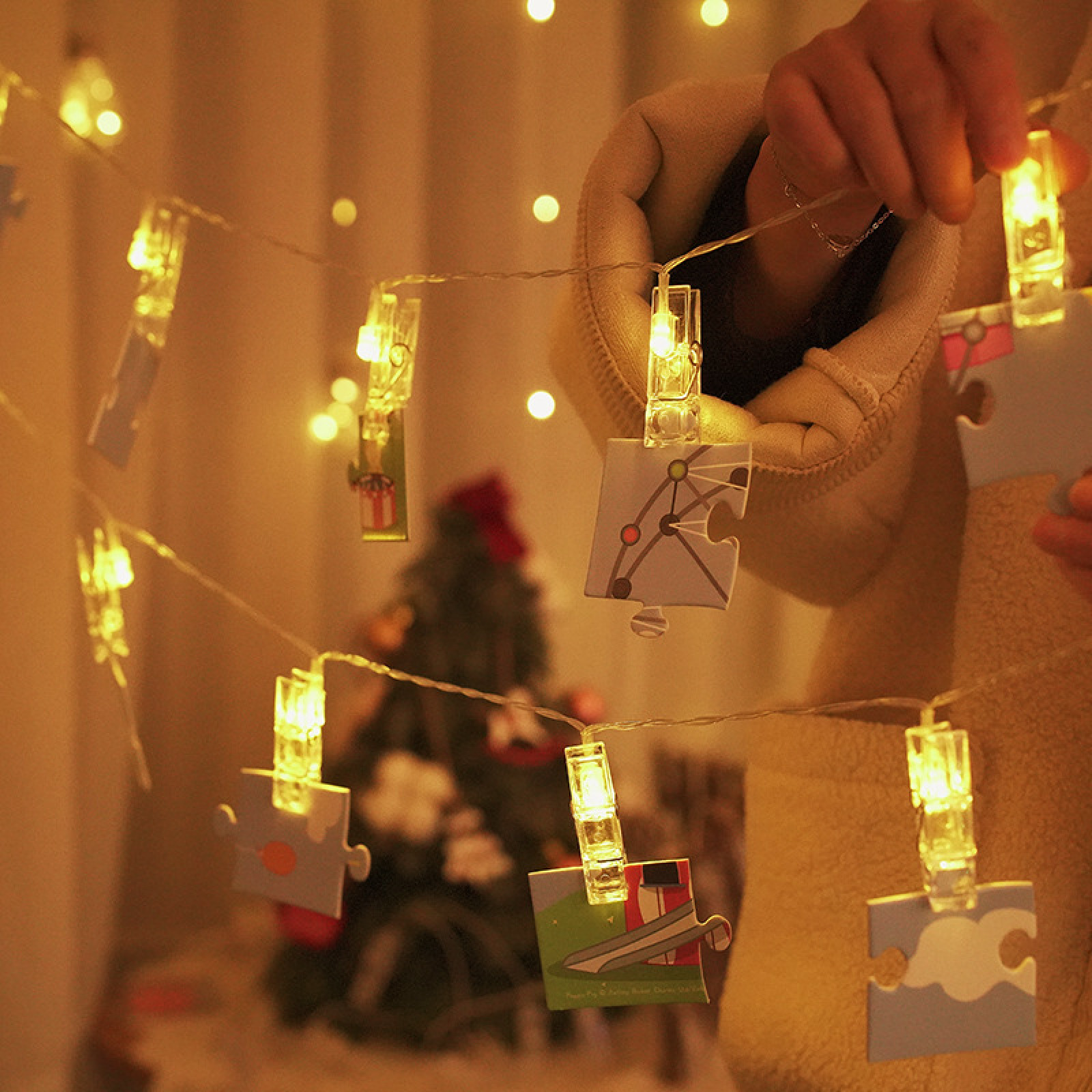 Eine Lichterkette mit Puzzle-Stücken, die mit Klammern befestigt sind. Im Hintergrund ein Weihnachtsbaum.