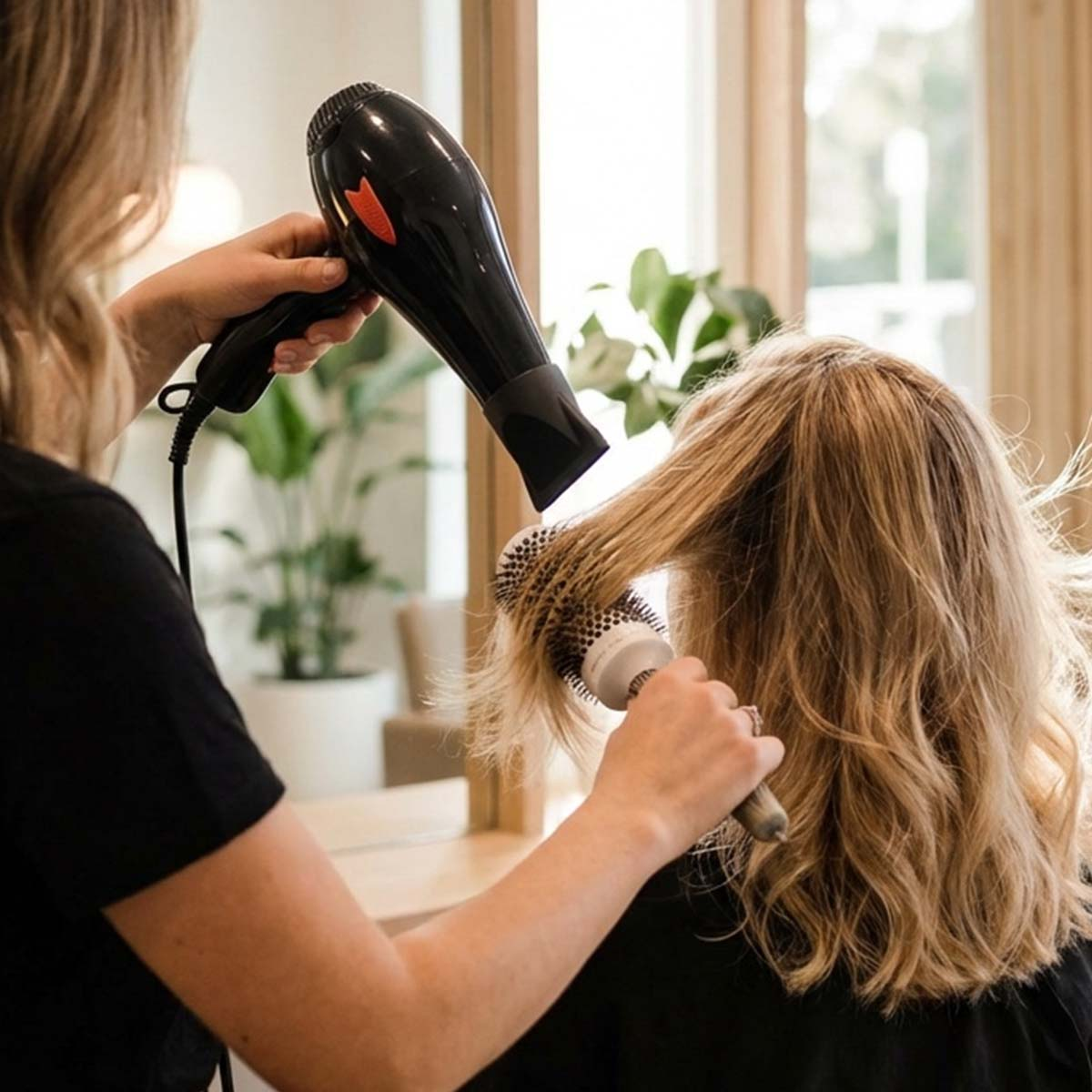 Eine Friseurin föhnt und bürstet die blonden Haare einer Kundin im Salon.