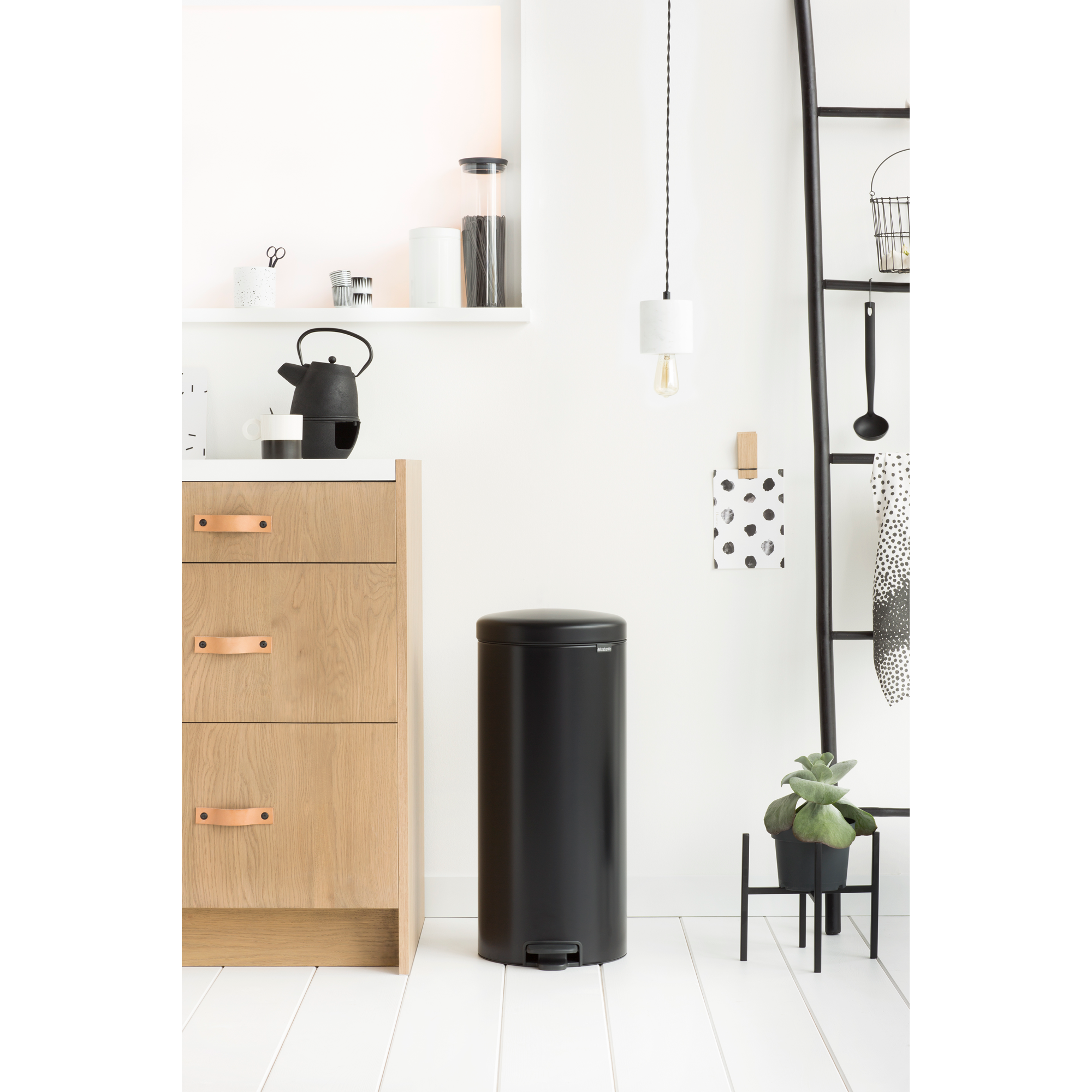Een zwarte pedaalemmer staat naast een houten kast in een keuken.