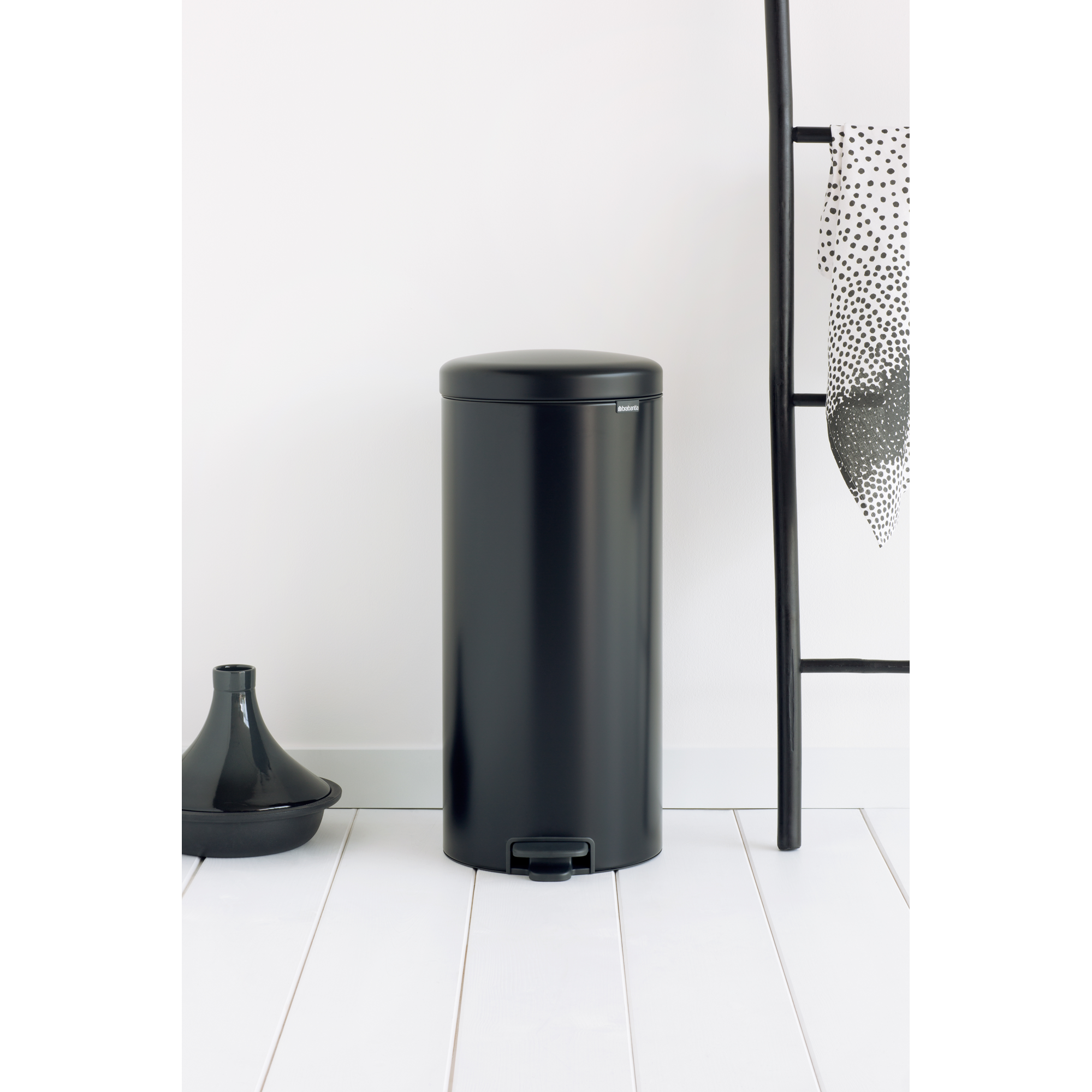 Een zwarte pedaalemmer naast een ladderrek met handdoek en pot.