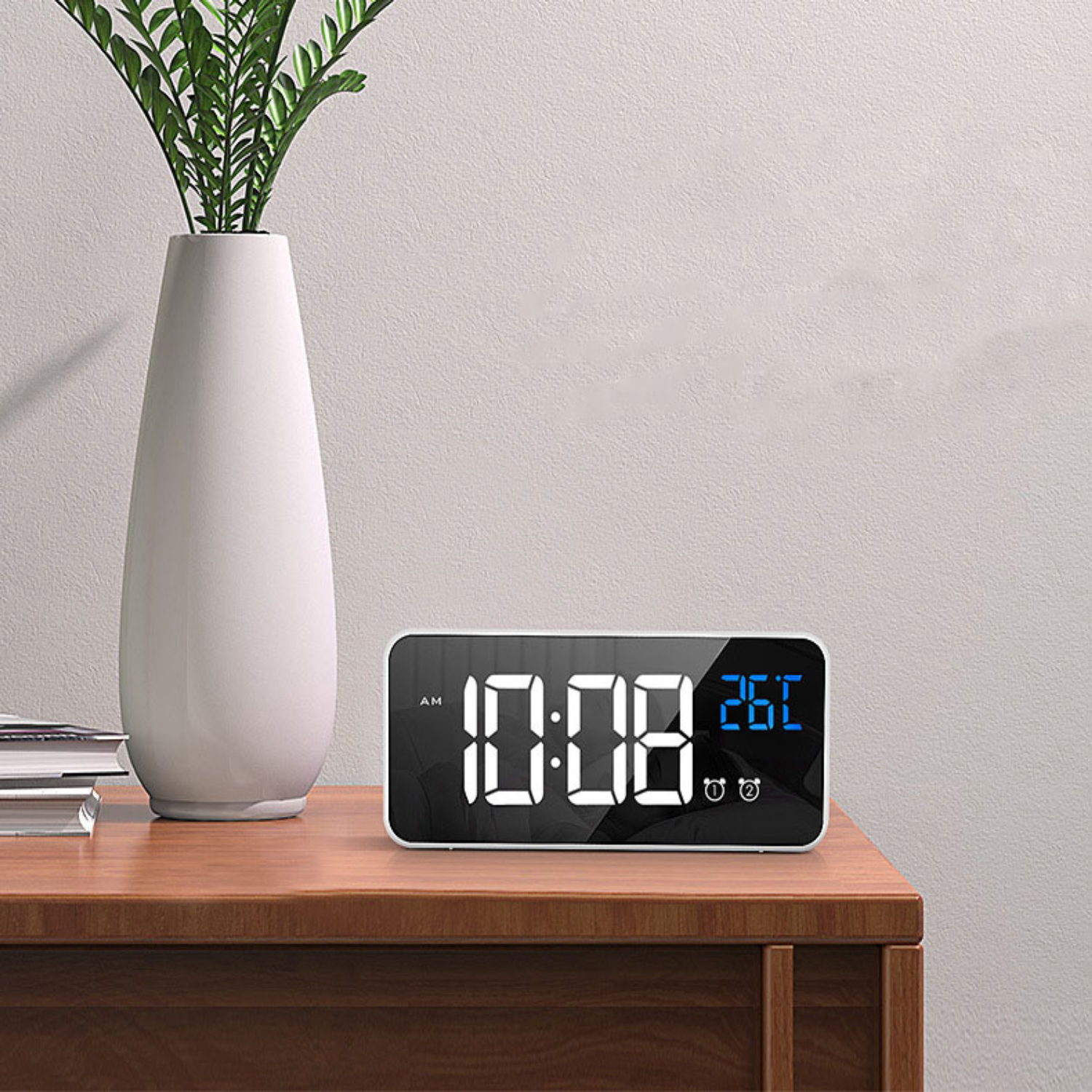 Ein digitaler Wecker zeigt 10:08 Uhr und 26°C auf einem Holztisch neben einer Vase.
