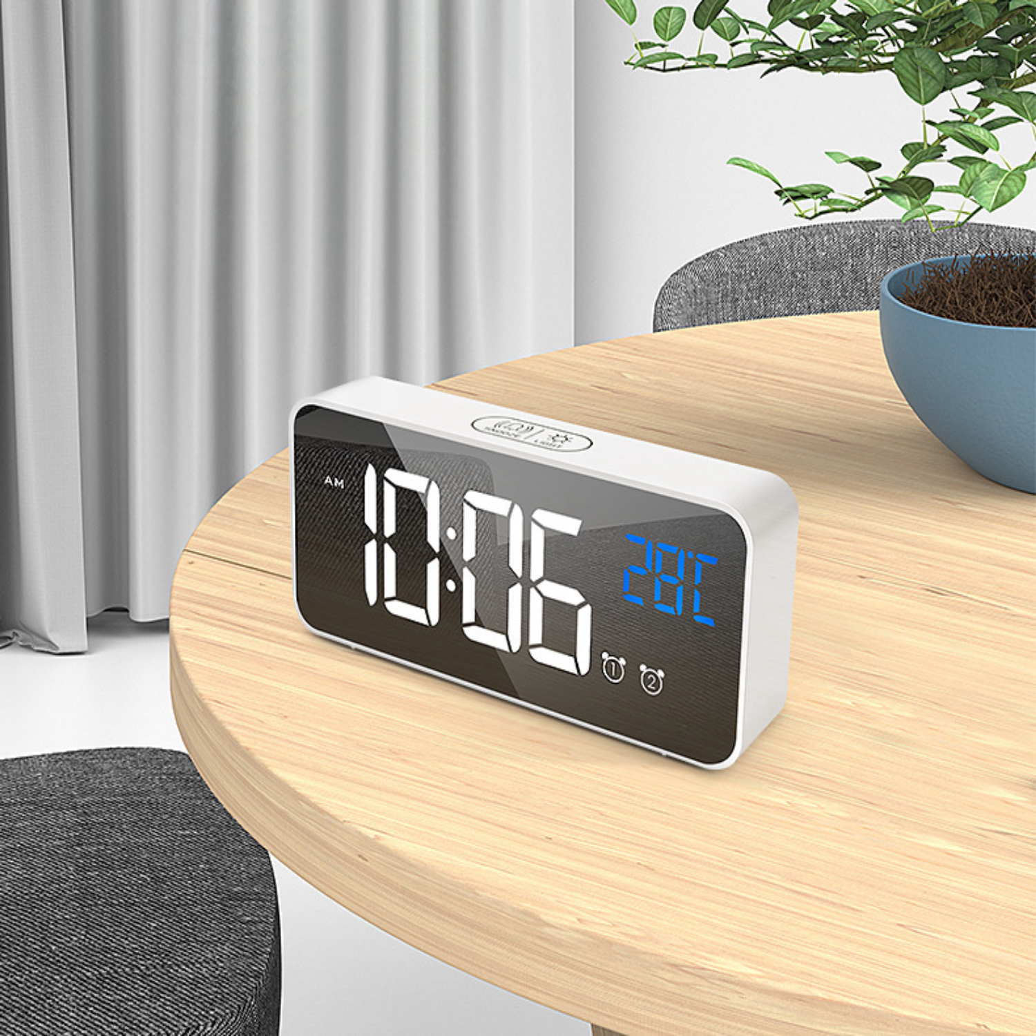 Ein weißer Digitalwecker zeigt 10:06 Uhr und 28 Grad Celsius auf einem Holztisch.