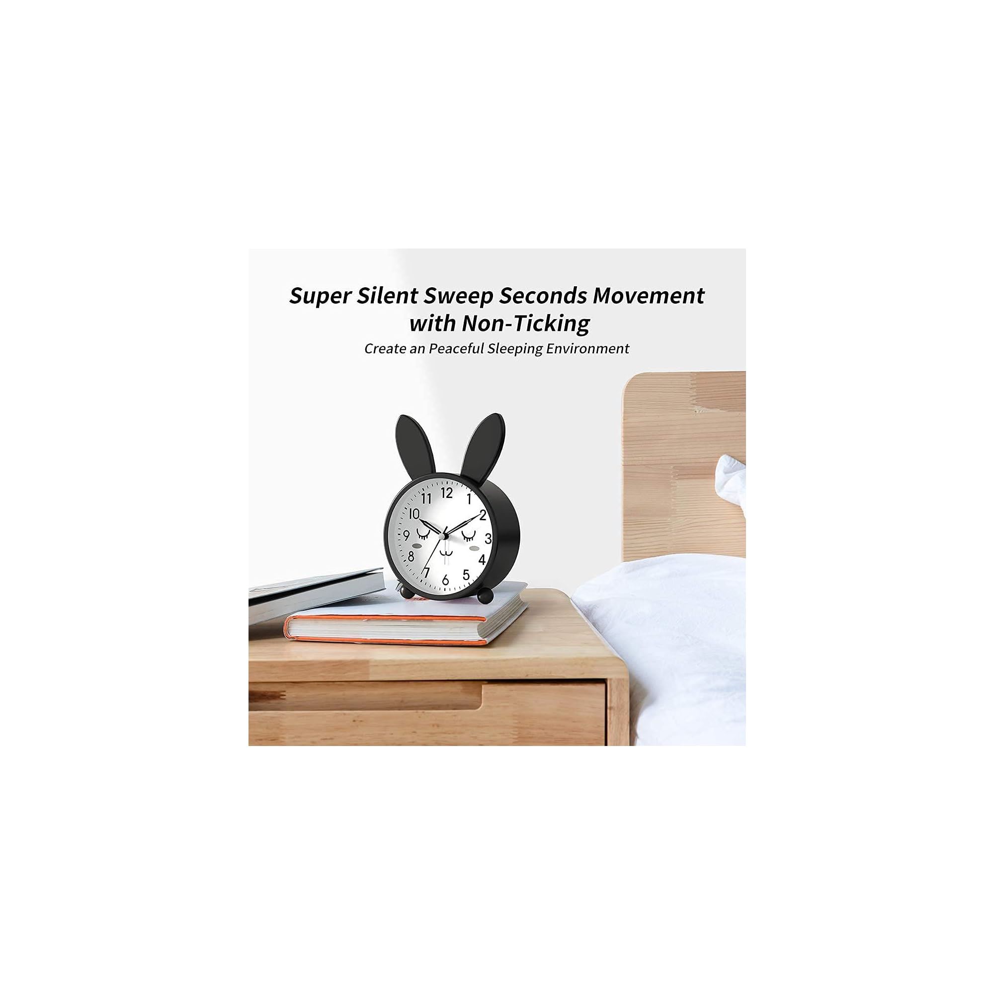 Ein schwarzer Wecker mit Hasenohren auf Büchern neben einem Bett.