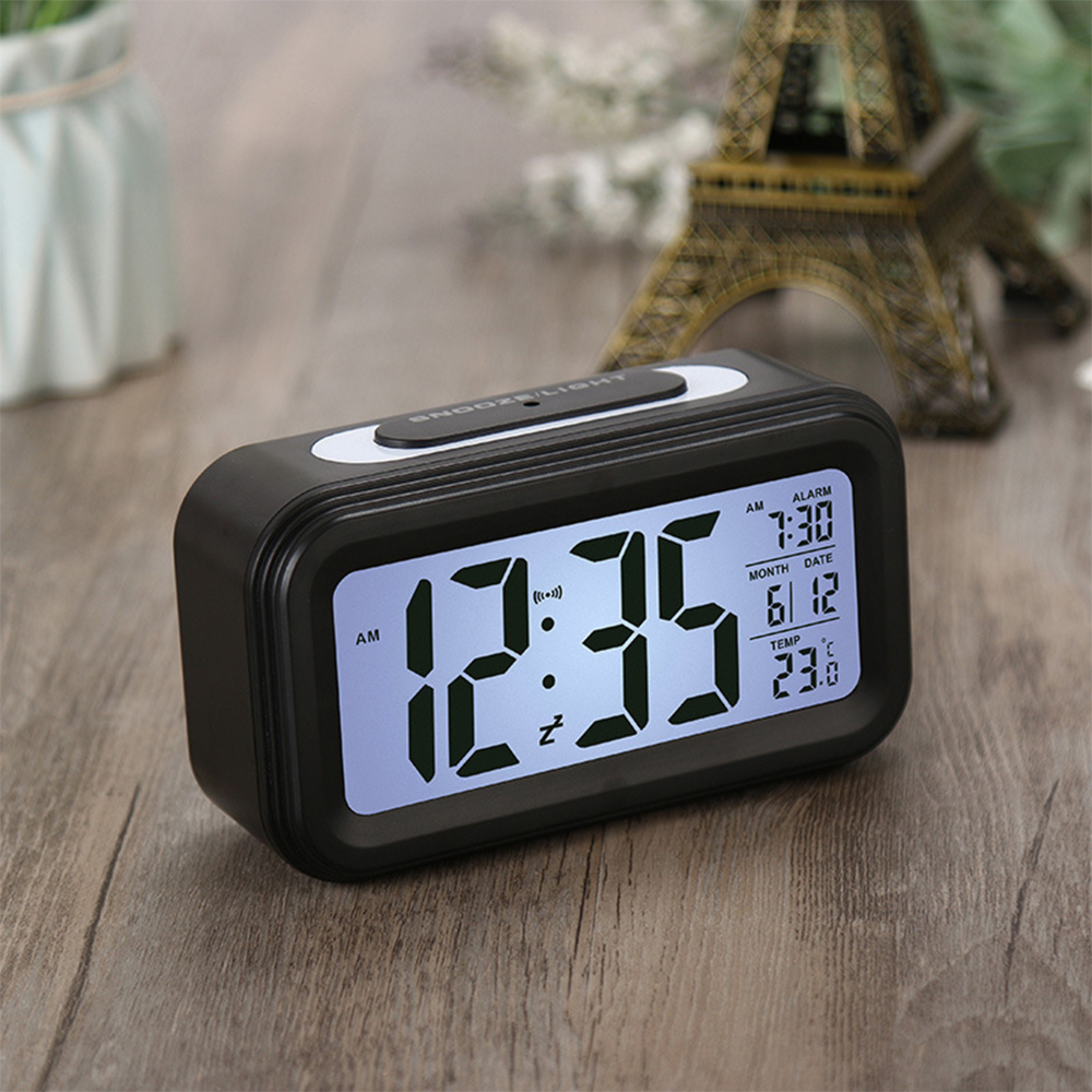 Ein schwarzer Digitalwecker auf einem Holztisch zeigt 12:35 Uhr, 7:30 Uhr Alarm und 23 Grad.