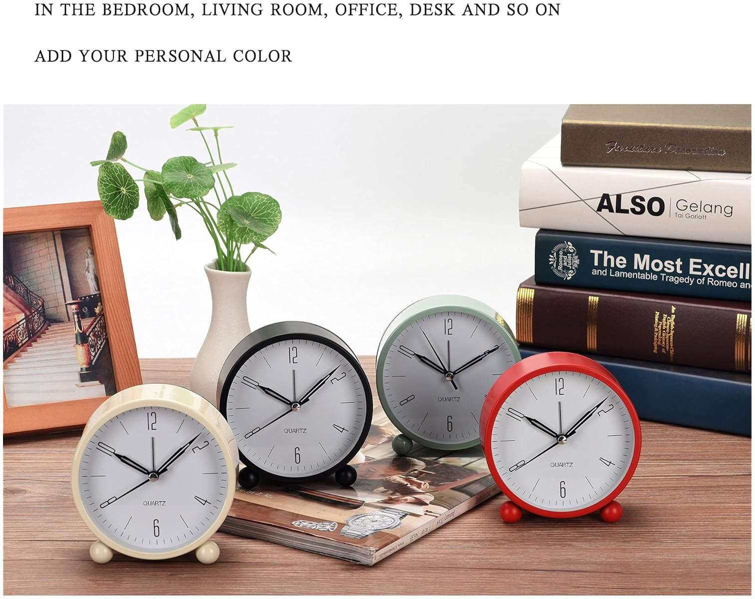 Vier Wecker in Creme, Schwarz, Grün und Rot stehen auf einem Tisch mit Büchern.