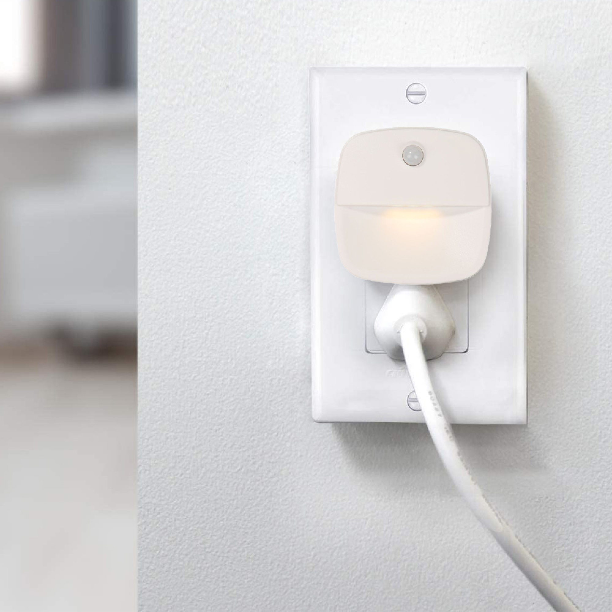 Ein weißer Nachtlicht-Sensorstecker mit warmem Licht in einer Steckdose.