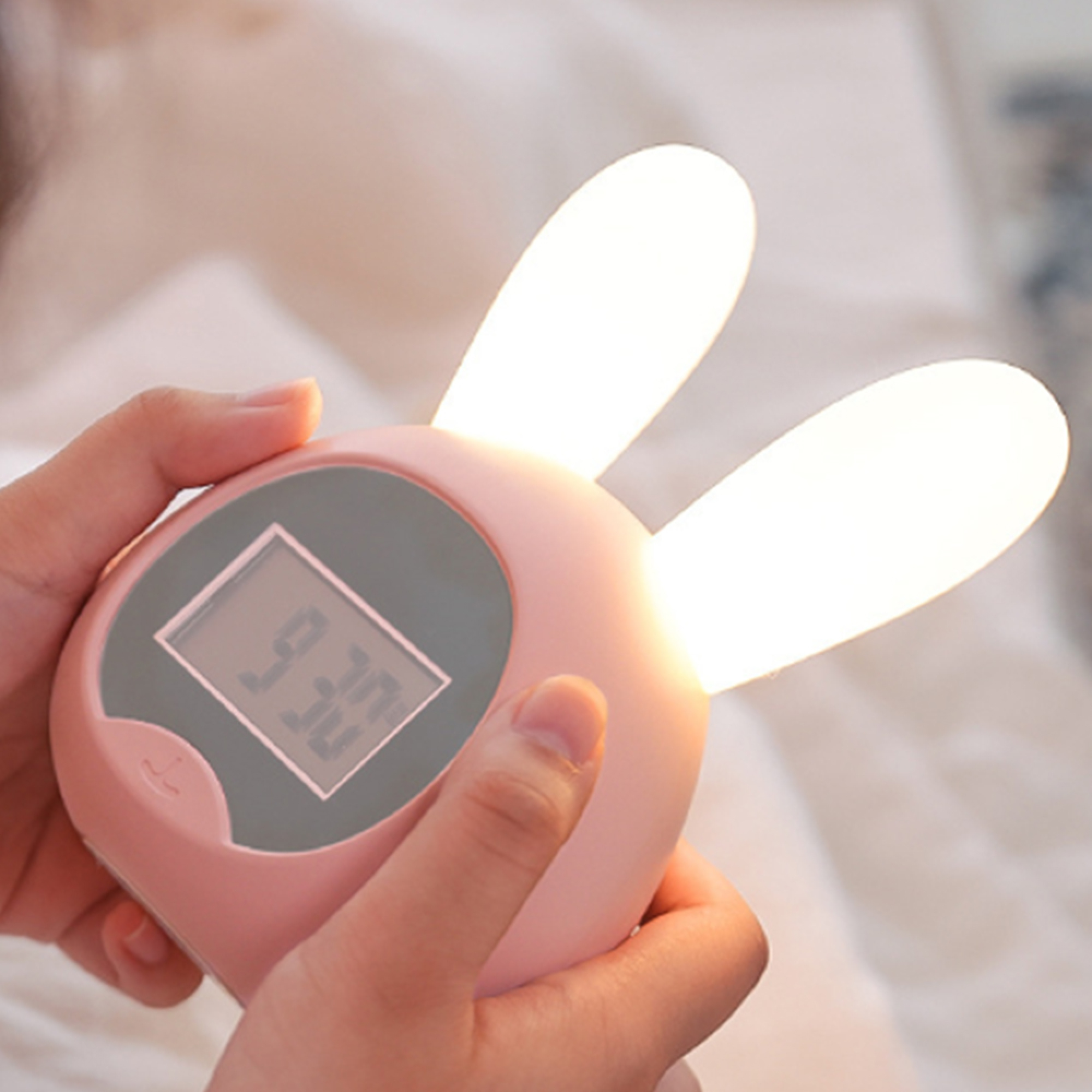 Eine Person hält einen rosa Wecker mit Hasenohren und einem digitalen Display.