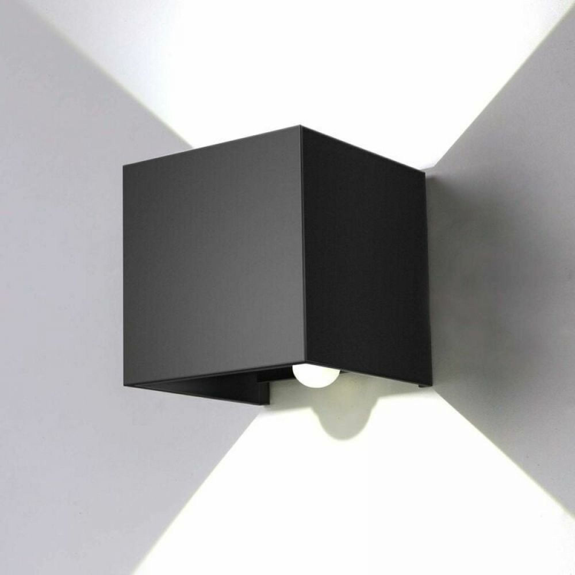 Eine schwarze Würfelwandleuchte mit einer sichtbaren Glühbirne leuchtet auf einer weißen Wand.