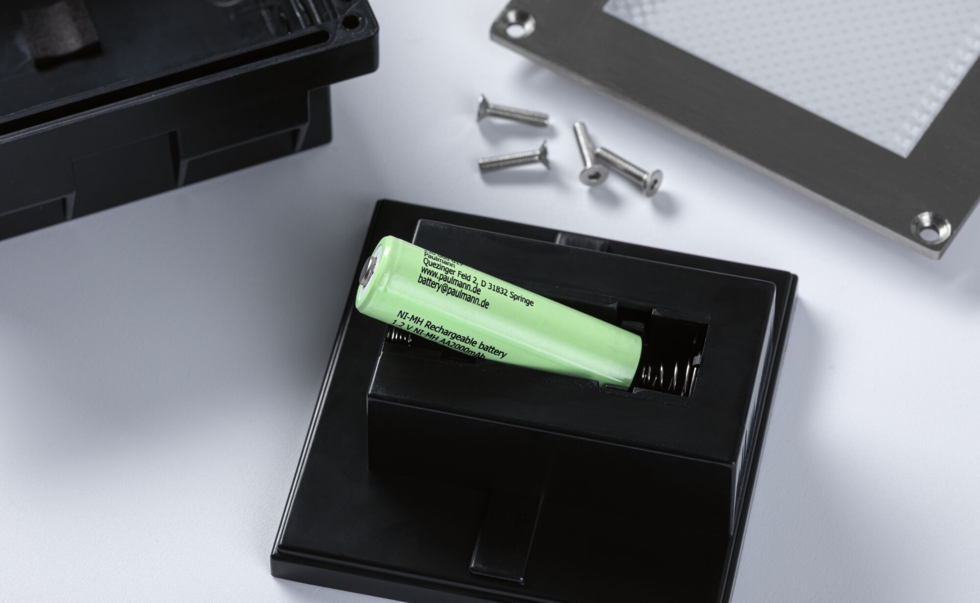 Grüne AA NiMH Batterie in schwarzem Fach, daneben Schrauben.