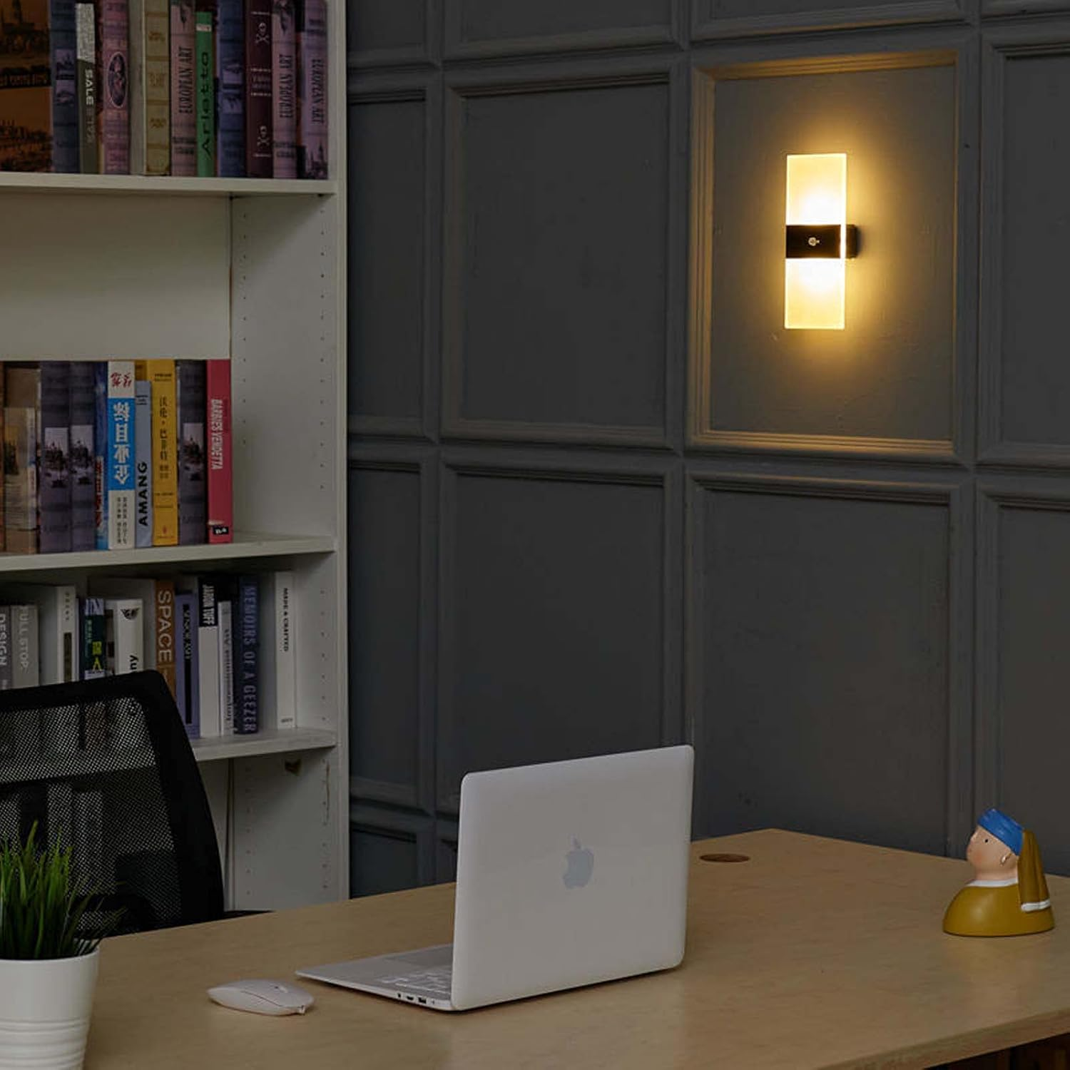 Ein Schreibtisch mit Laptop, Maus, Lampe und Bücherregal.