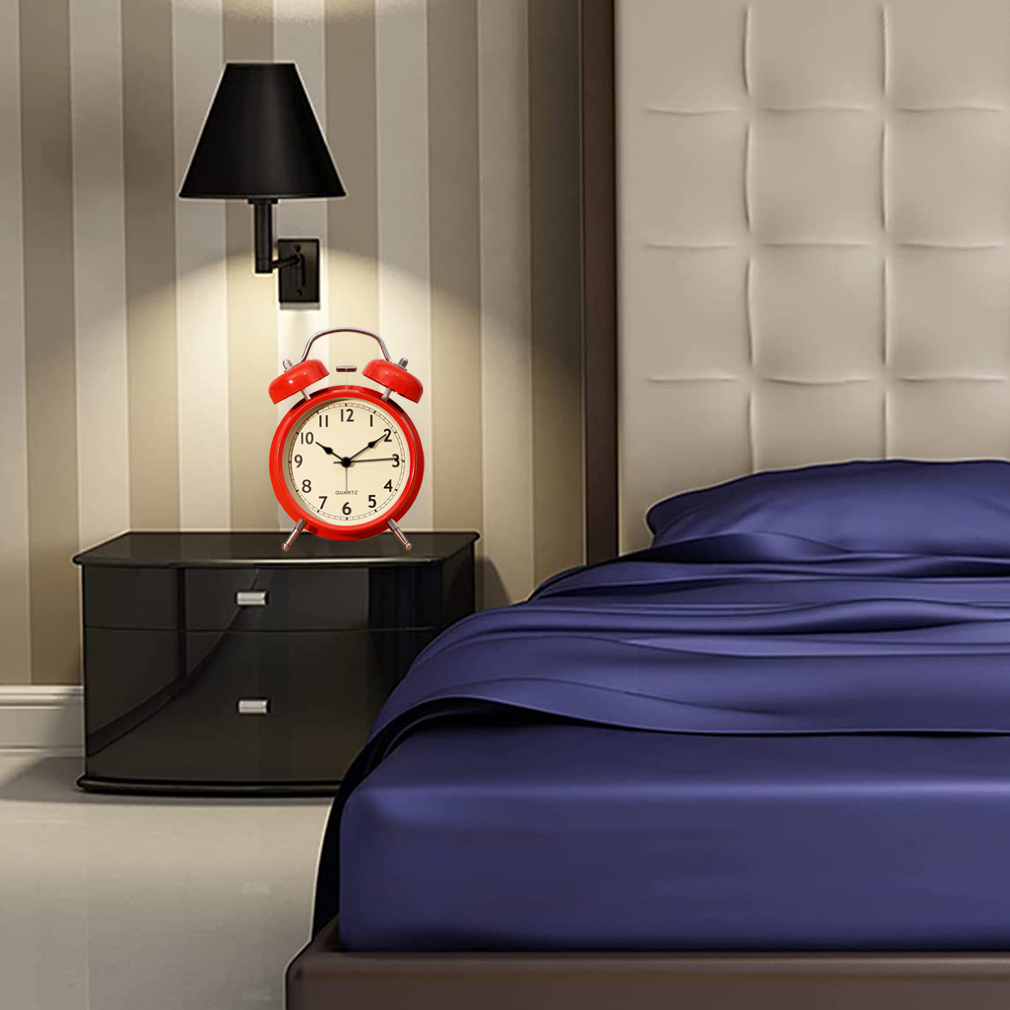 Ein roter Wecker auf einem schwarzen Nachttisch neben einem Bett mit blauer Bettwäsche.