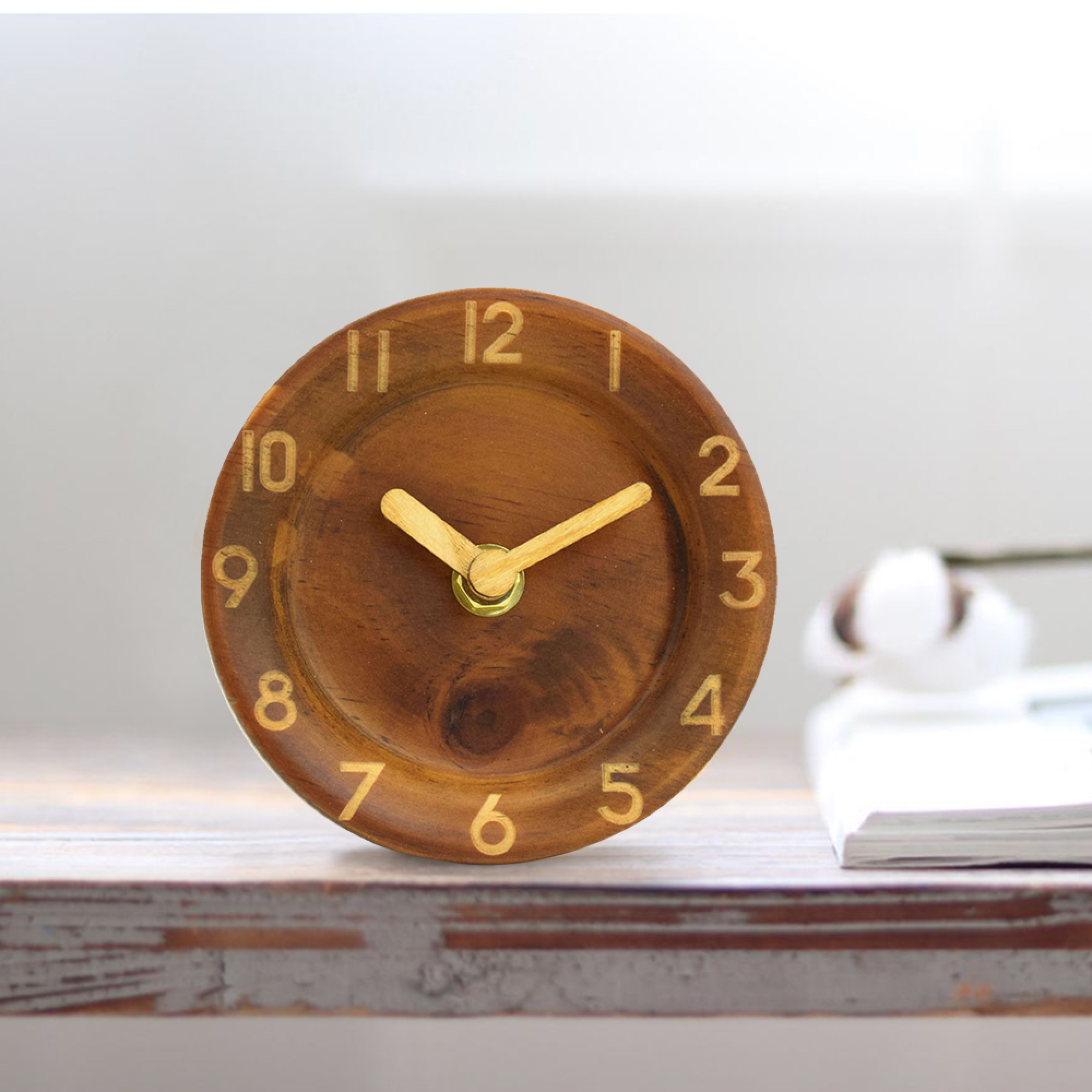 Ein runder Holzwecker mit goldenen Zeigern und Ziffern auf einem Tisch.
