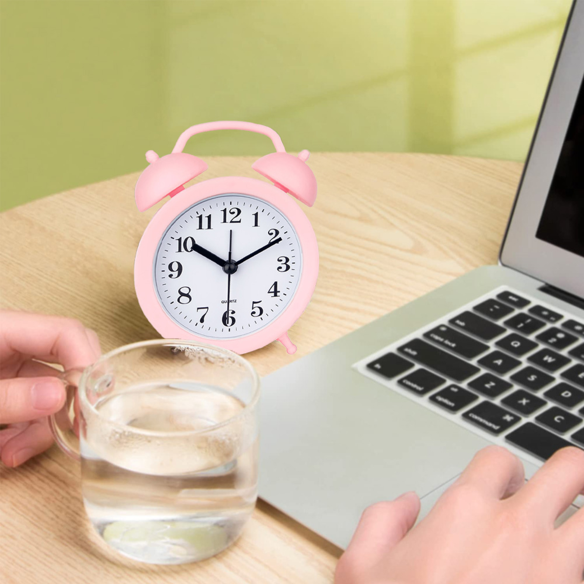 Rosa Wecker auf einem Holztisch neben einem Laptop und einem Glas Wasser.