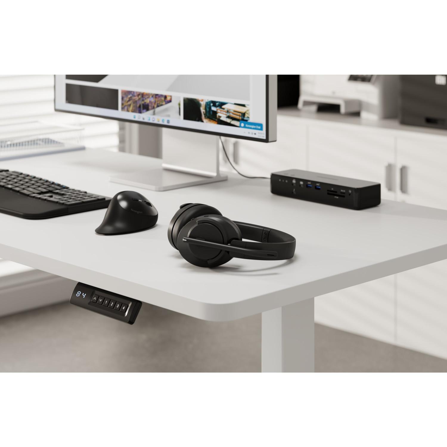 Una scrivania con monitor, tastiera, mouse, cuffie e docking station.