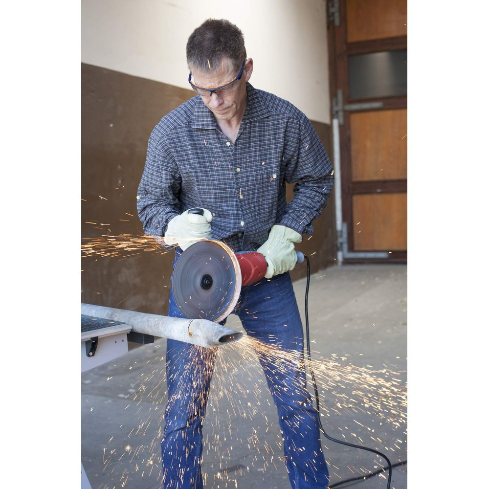 Mann mit Schutzbrille und Handschuhen schneidet Metallrohr mit Winkelschleifer, Funken sprühen.