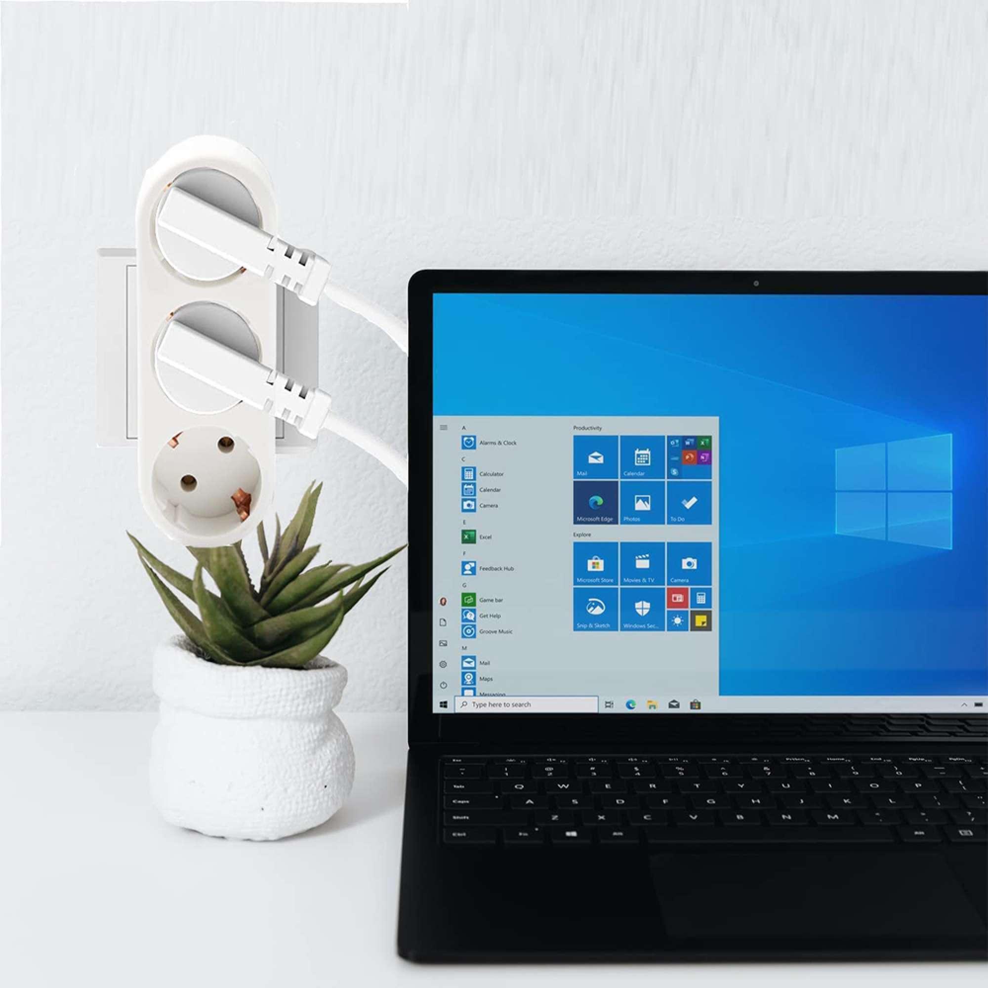 Ein Laptop mit offenem Bildschirm steht neben einer Steckdosenleiste und einer Topfpflanze.