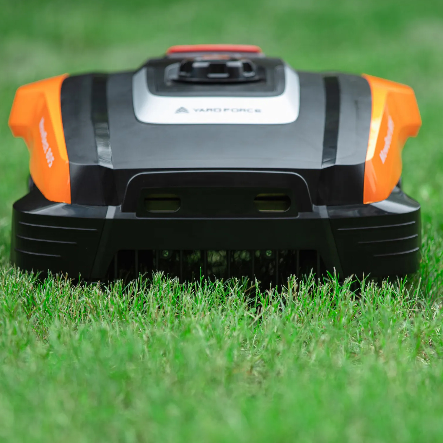 Ein schwarzer und oranger Mähroboter steht auf saftigem, grünem Gras.