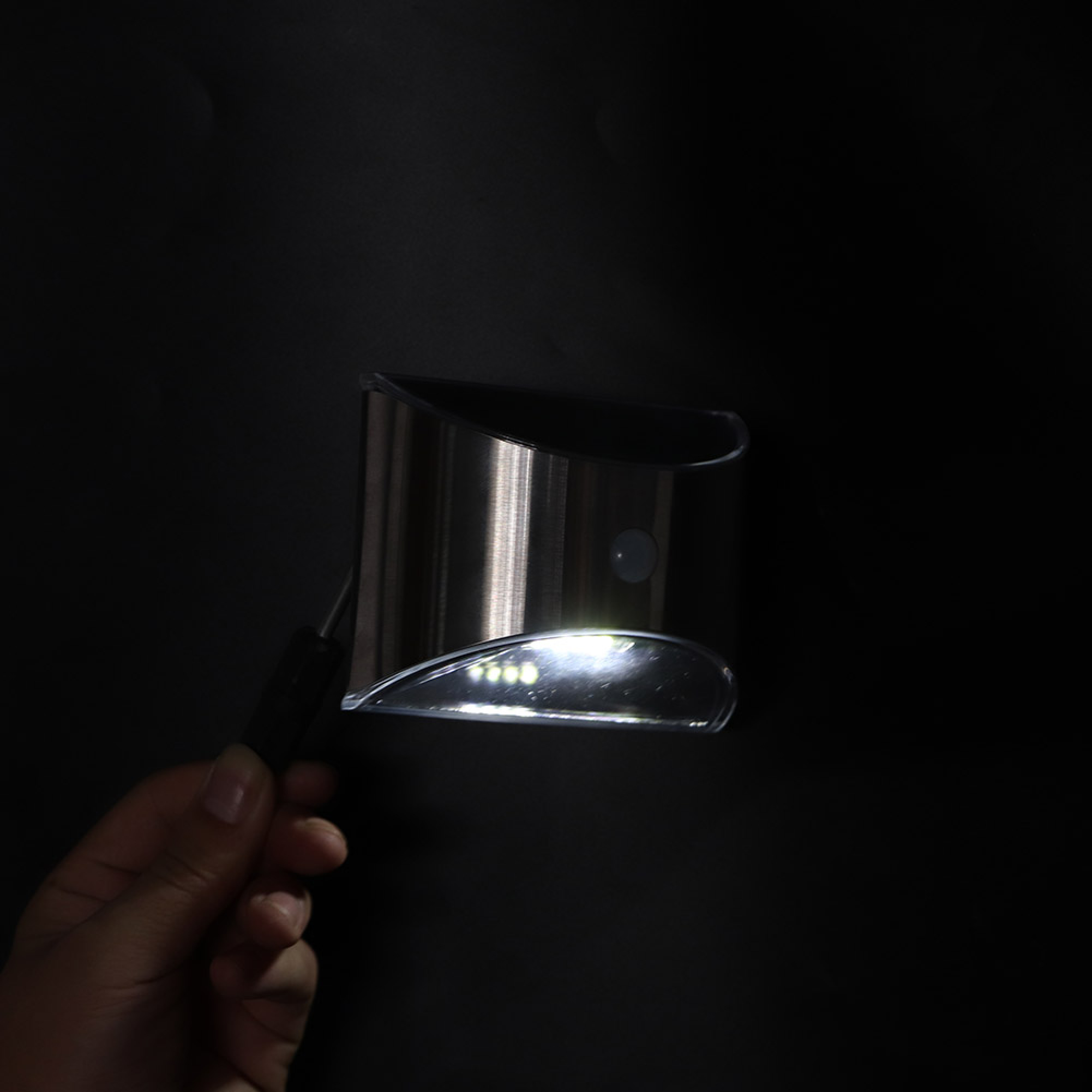 Eine Hand hält eine silberne Solarleuchte mit weißen LEDs vor schwarzem Hintergrund.