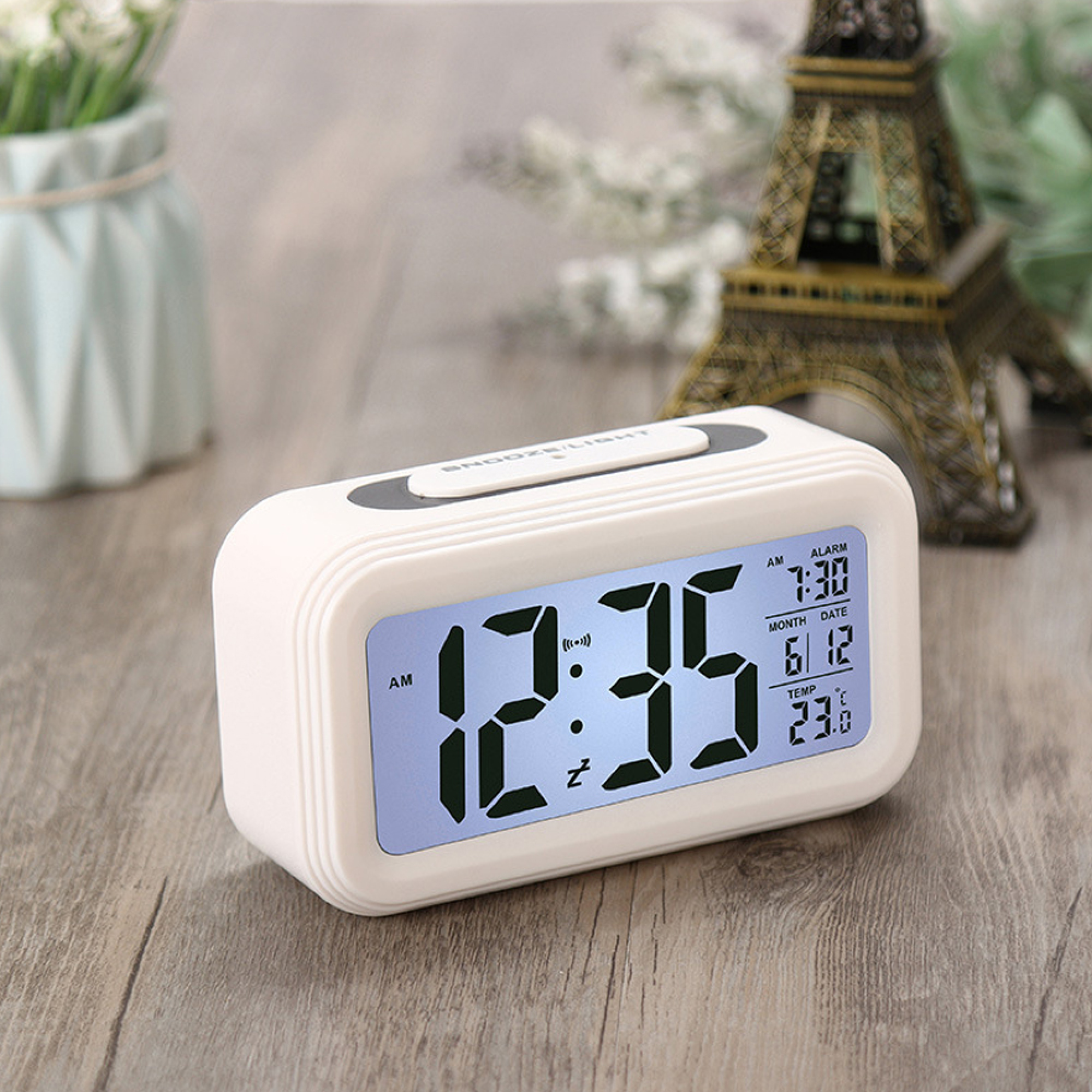 Ein weißer digitaler Wecker auf einem Holztisch zeigt 12:35 Uhr an.