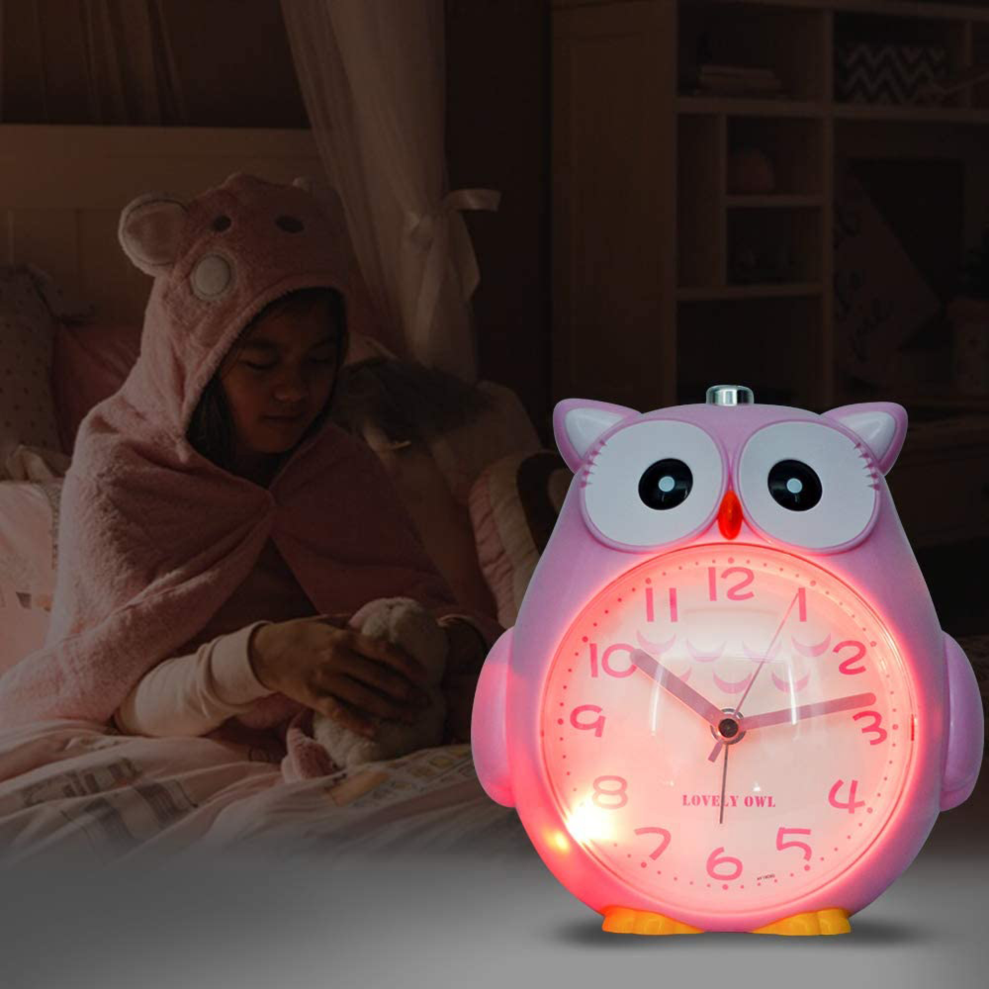 Ein rosafarbener Uhrenwecker in Eulenform leuchtet rot. Ein Kind in einem Bären-Hoodie liegt im Bett.