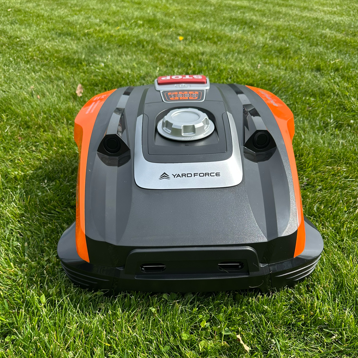 Ein orange-schwarzer Mähroboter steht auf einem grünen Rasen.