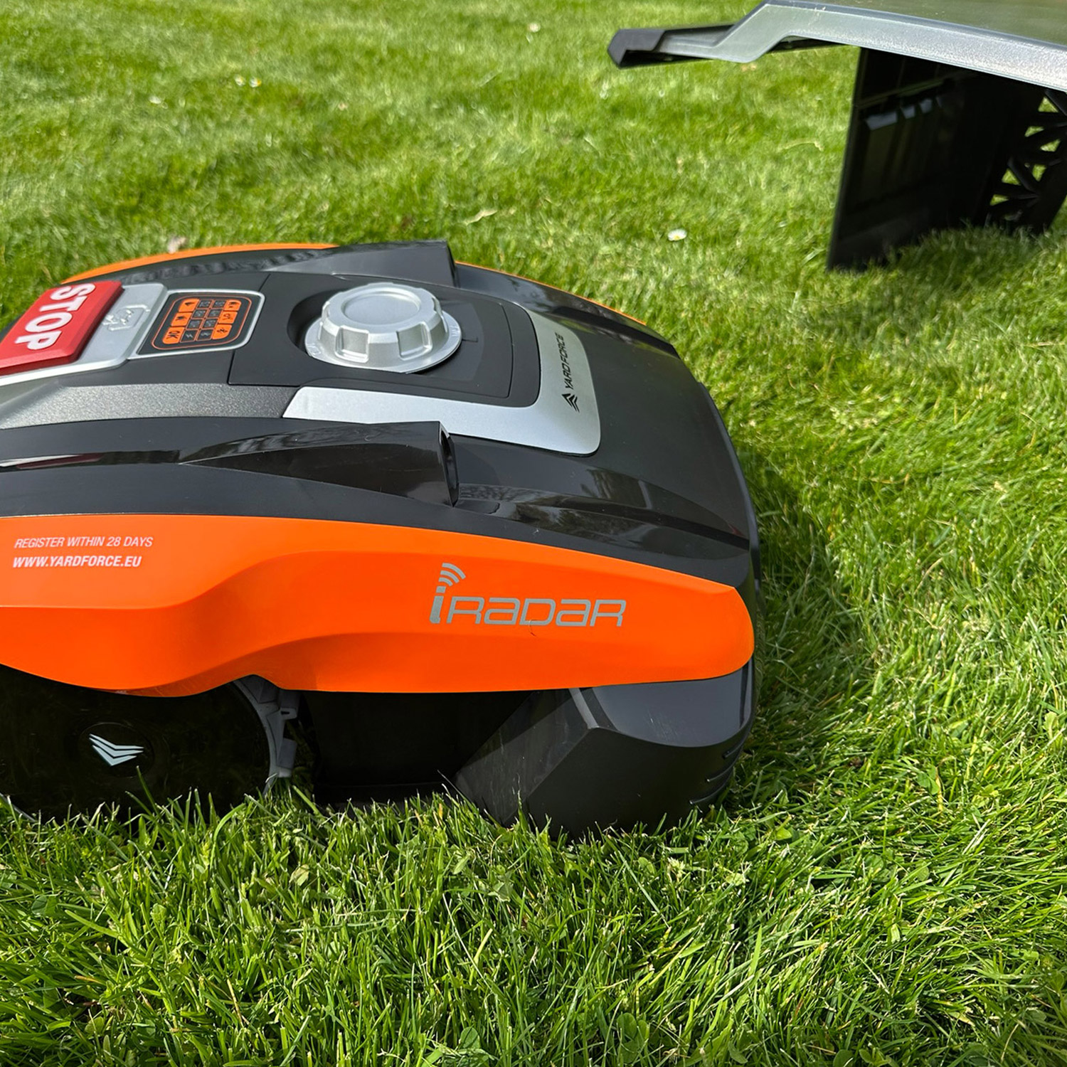 Ein schwarzer und oranger Mähroboter mit "STOP"-Taste auf einem grünen Rasen.