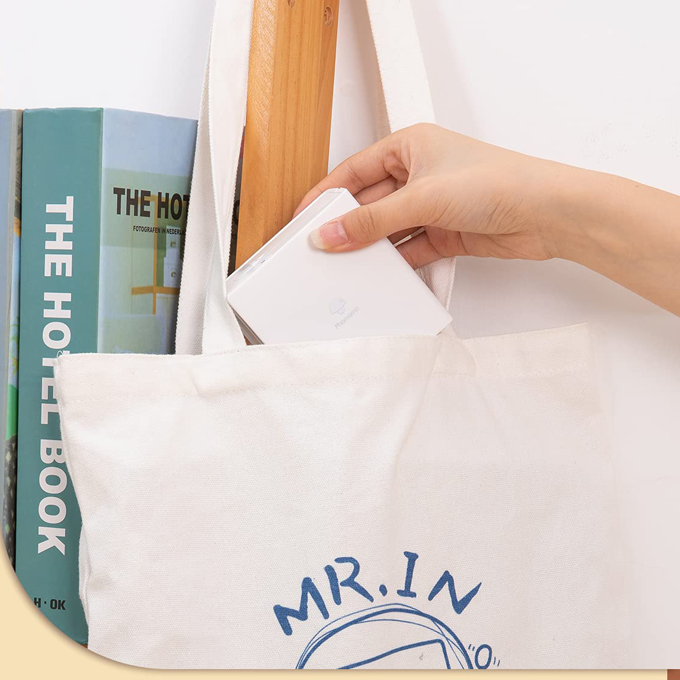 Eine Hand legt ein weißes Ladegerät in eine weiße Stofftasche neben Büchern.