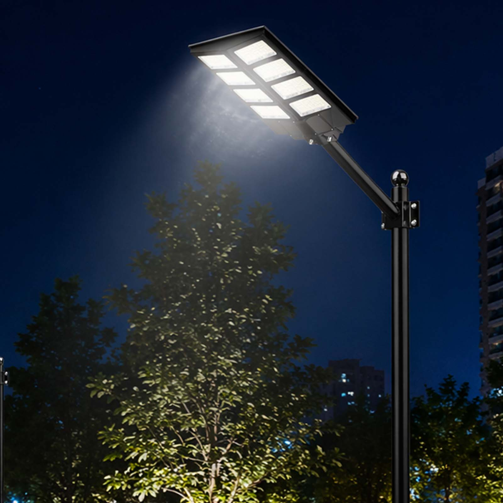 Eine moderne LED-Straßenlaterne leuchtet im Dunkeln, Bäume und Gebäude im Hintergrund.