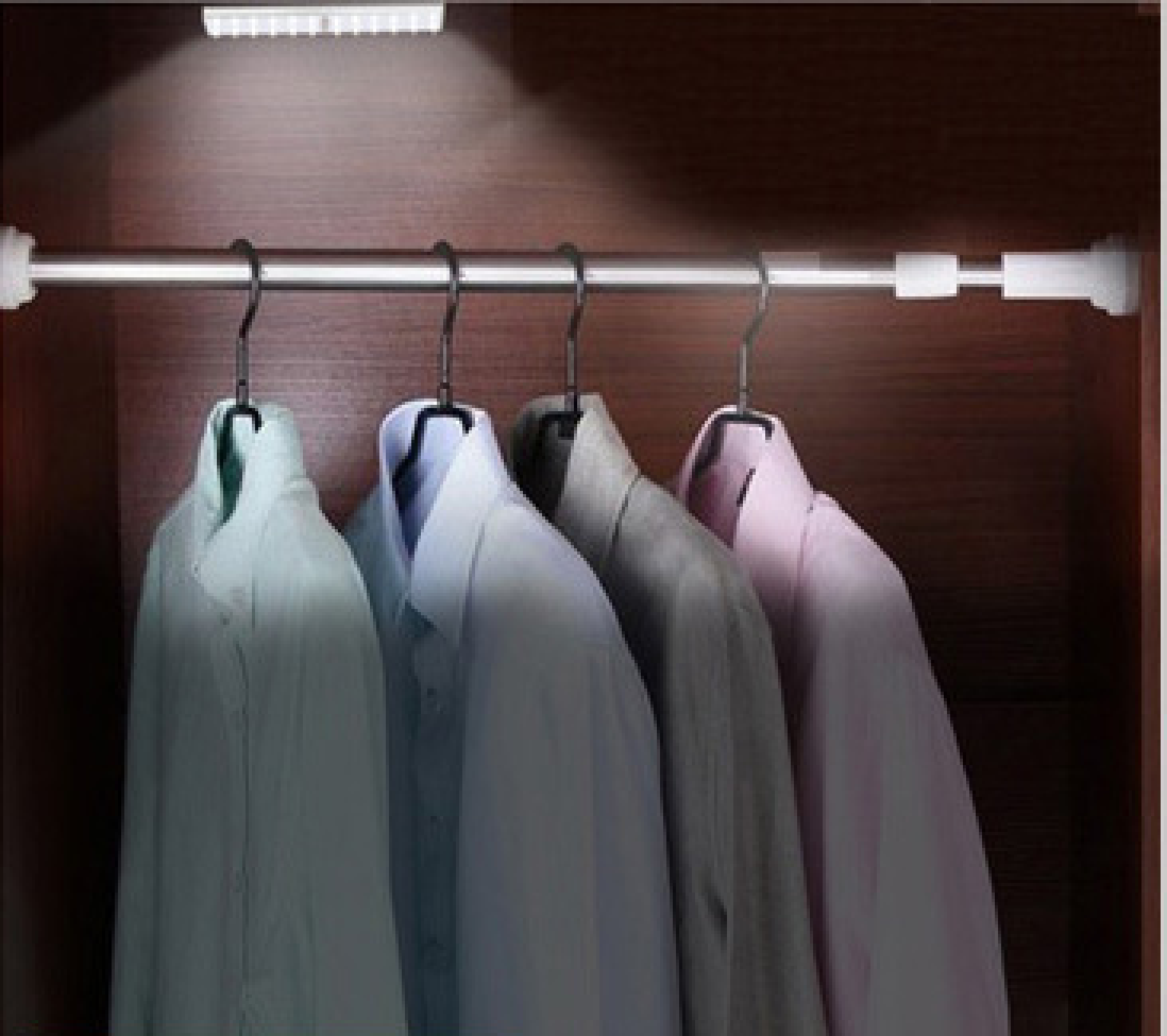 Ein Kleiderschrank mit vier Hemden an Bügeln, beleuchtet von einer LED-Leiste.