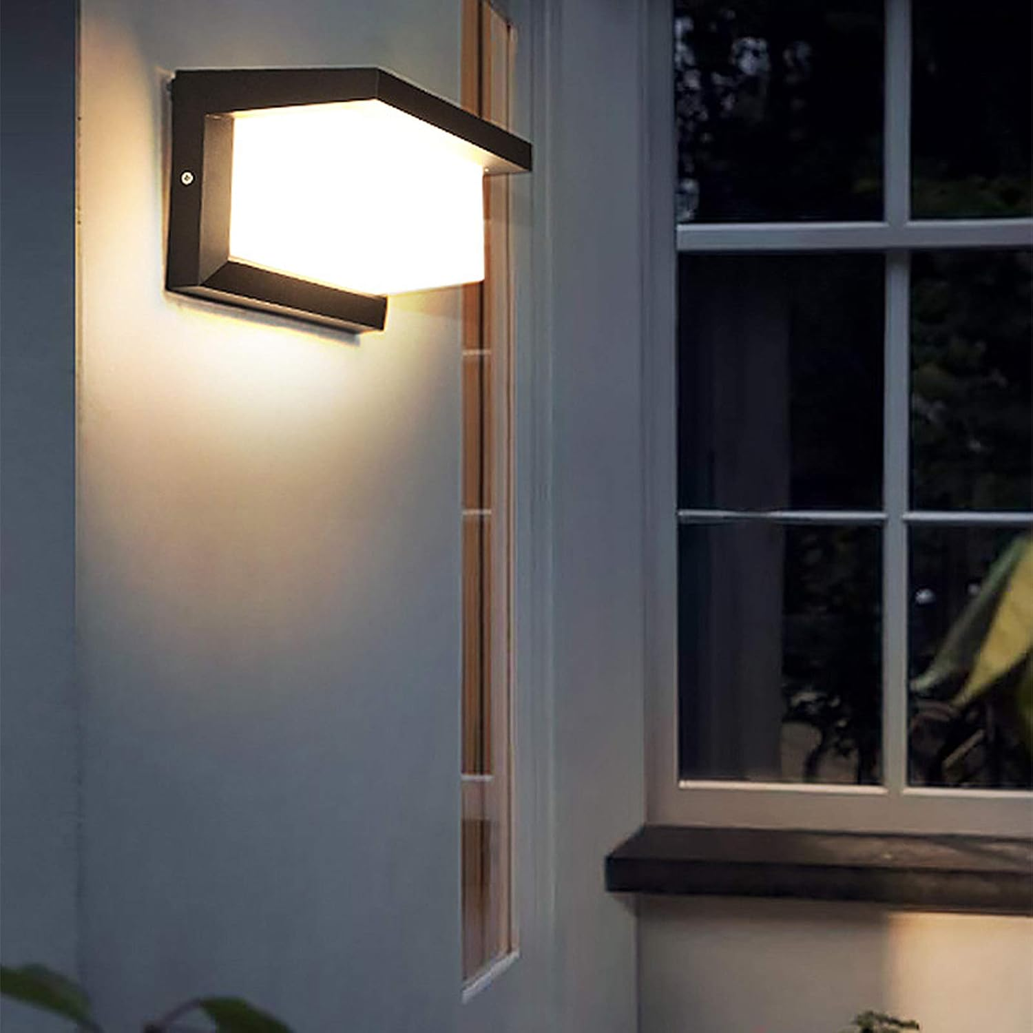 Ein moderner Wandleuchter beleuchtet eine Wand neben einem Fenster bei Nacht.