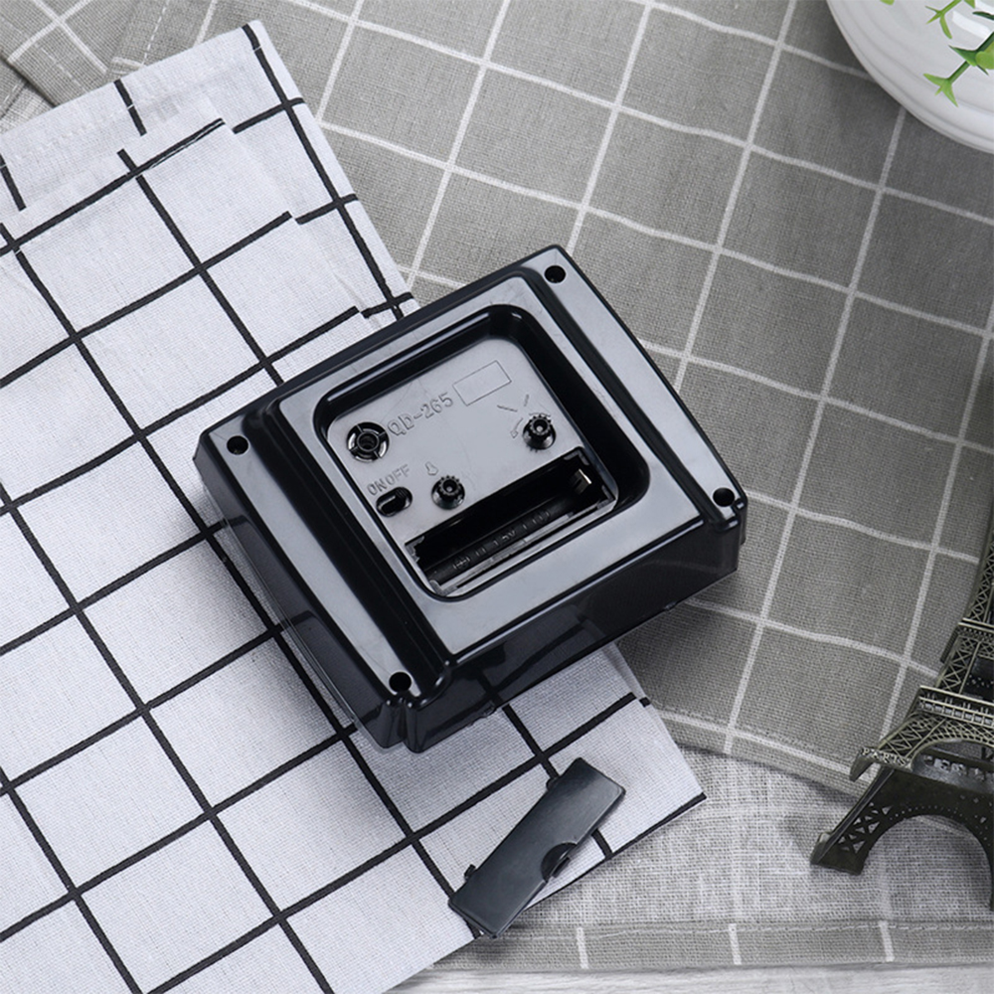 Rückseite eines schwarzen Geräts mit Batteriefach auf kariertem Stoff.