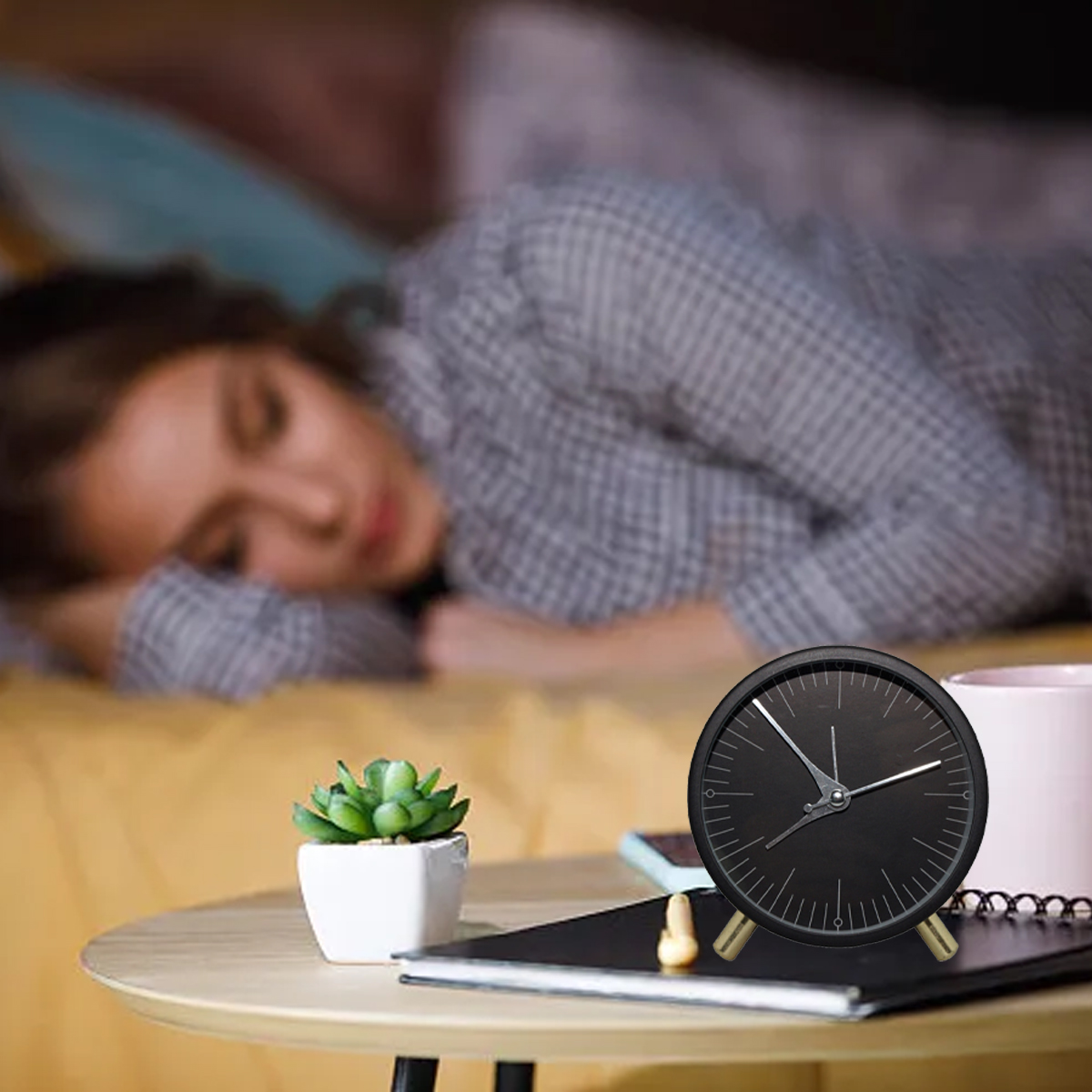 Eine Frau schläft im Bett, mit Wecker, Pflanze und Notizbuch auf einem Beistelltisch.