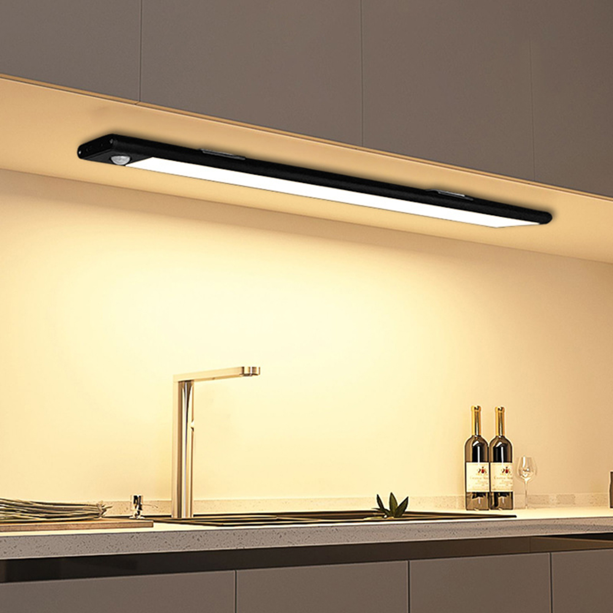 Eine lange, schmale schwarze Leuchte mit Bewegungsmelder über einer Küchenarbeitsplatte mit Wasserhahn, Flaschen und Glas.