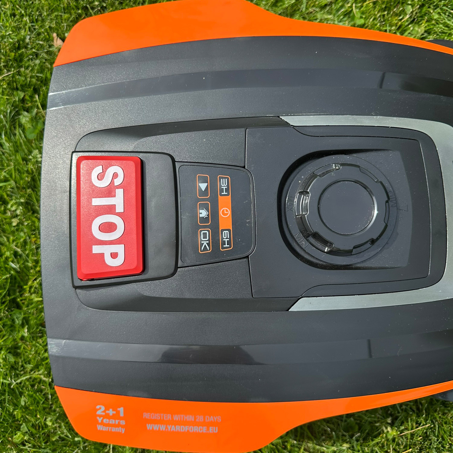Mähroboter mit rotem STOP-Knopf auf Gras. Orange-grauer Korpus.
