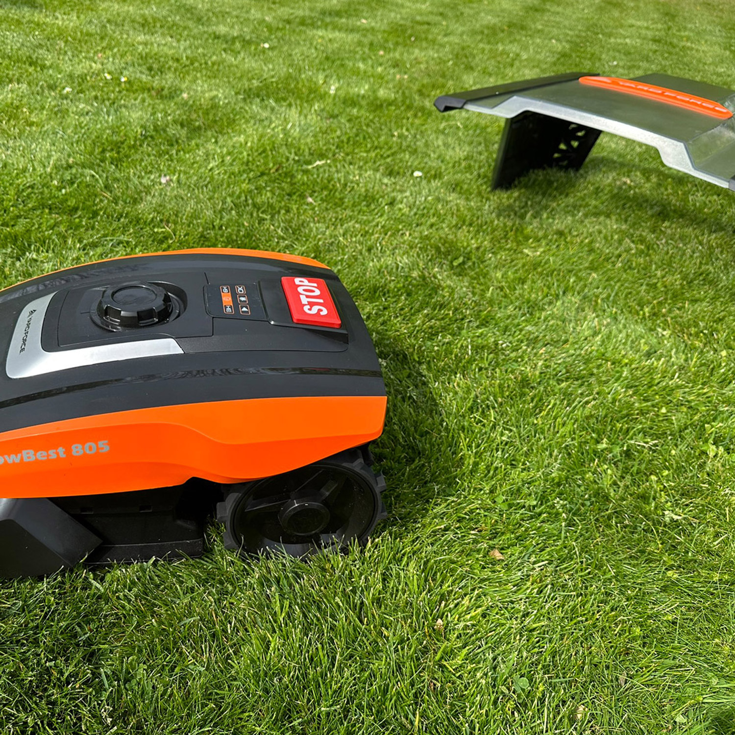Ein orange-schwarzer Mähroboter steht auf einem Rasen. Ein zweiter Roboter ist im Hintergrund.