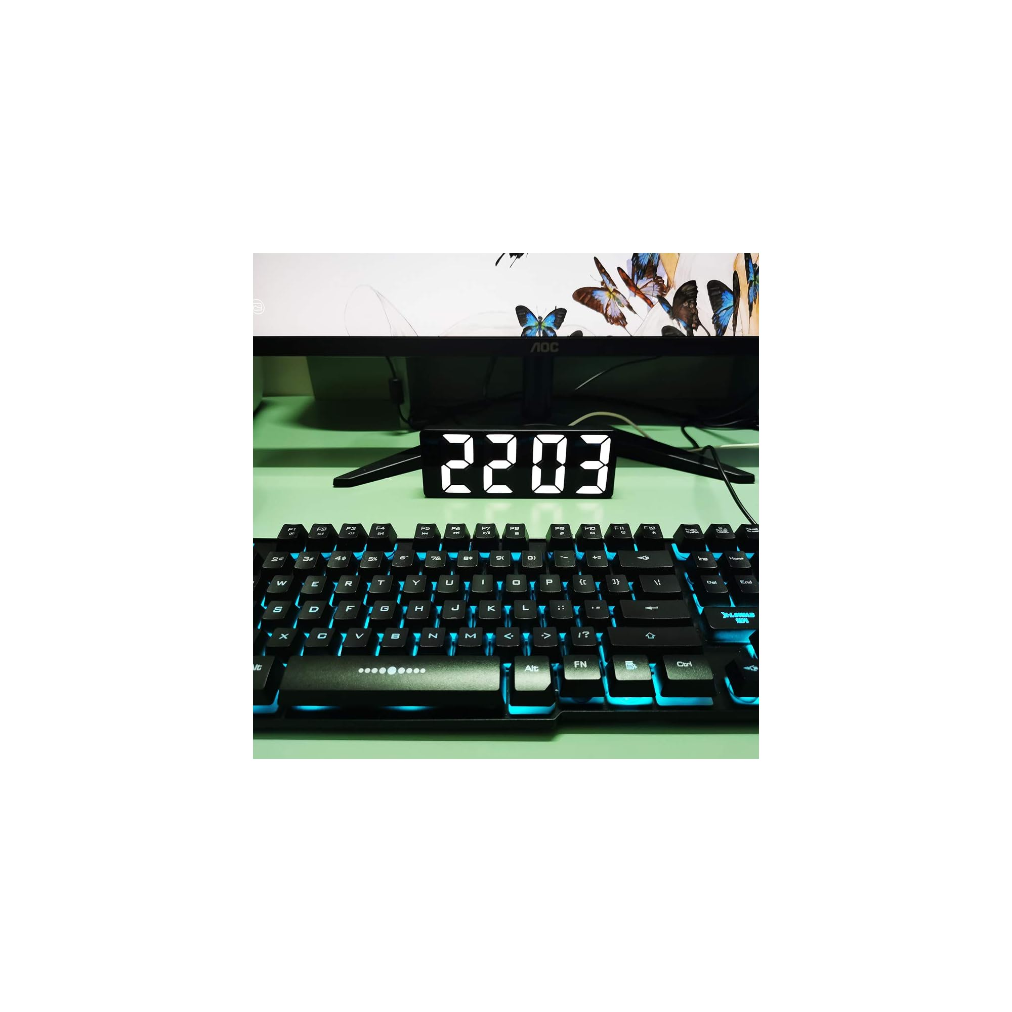 Ein digitaler Wecker zeigt 22:03 an, vor einer Tastatur und einem Monitor mit Schmetterlingen.